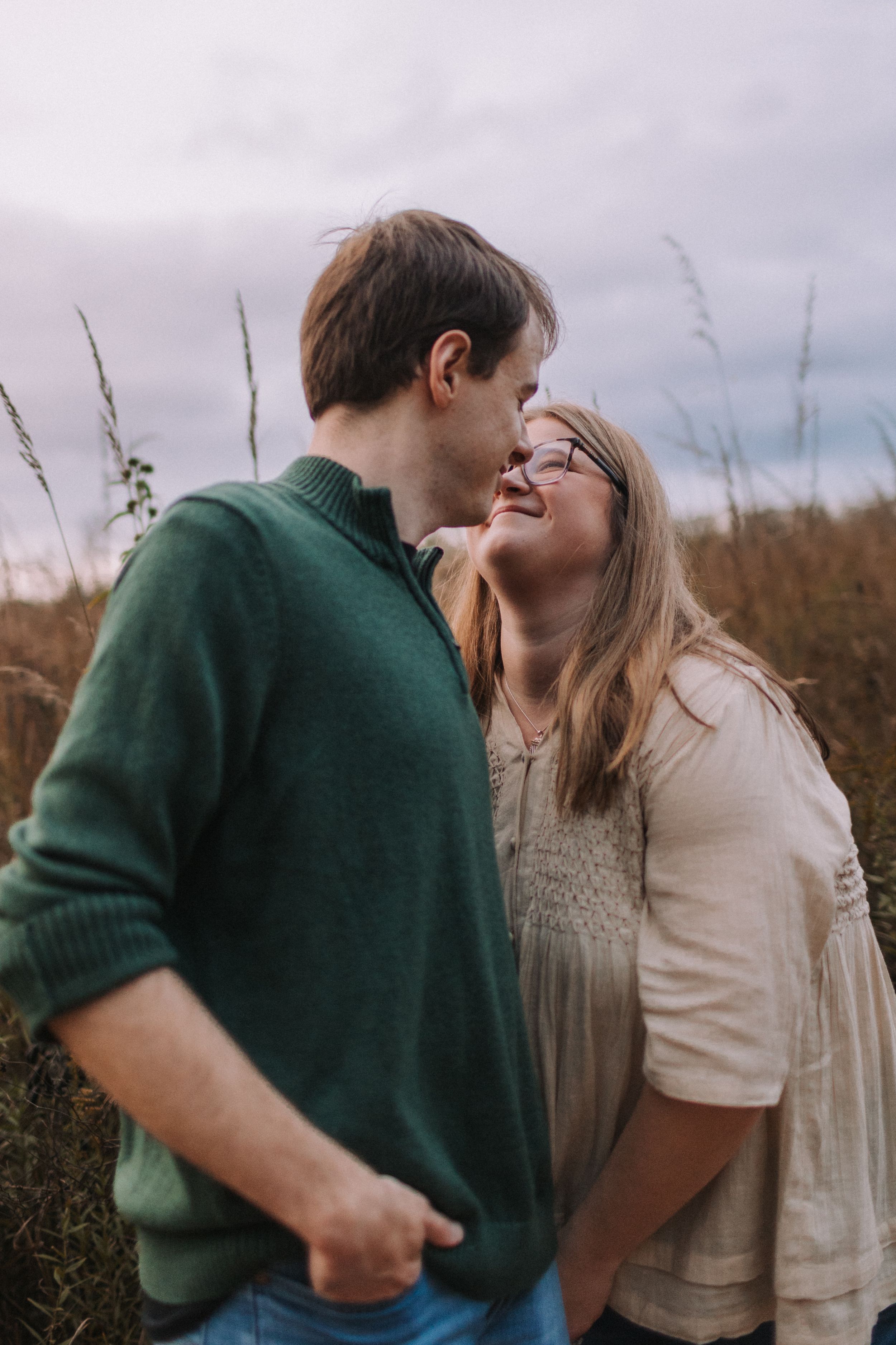 A tender moment between a couple standing in a field of tall grass.