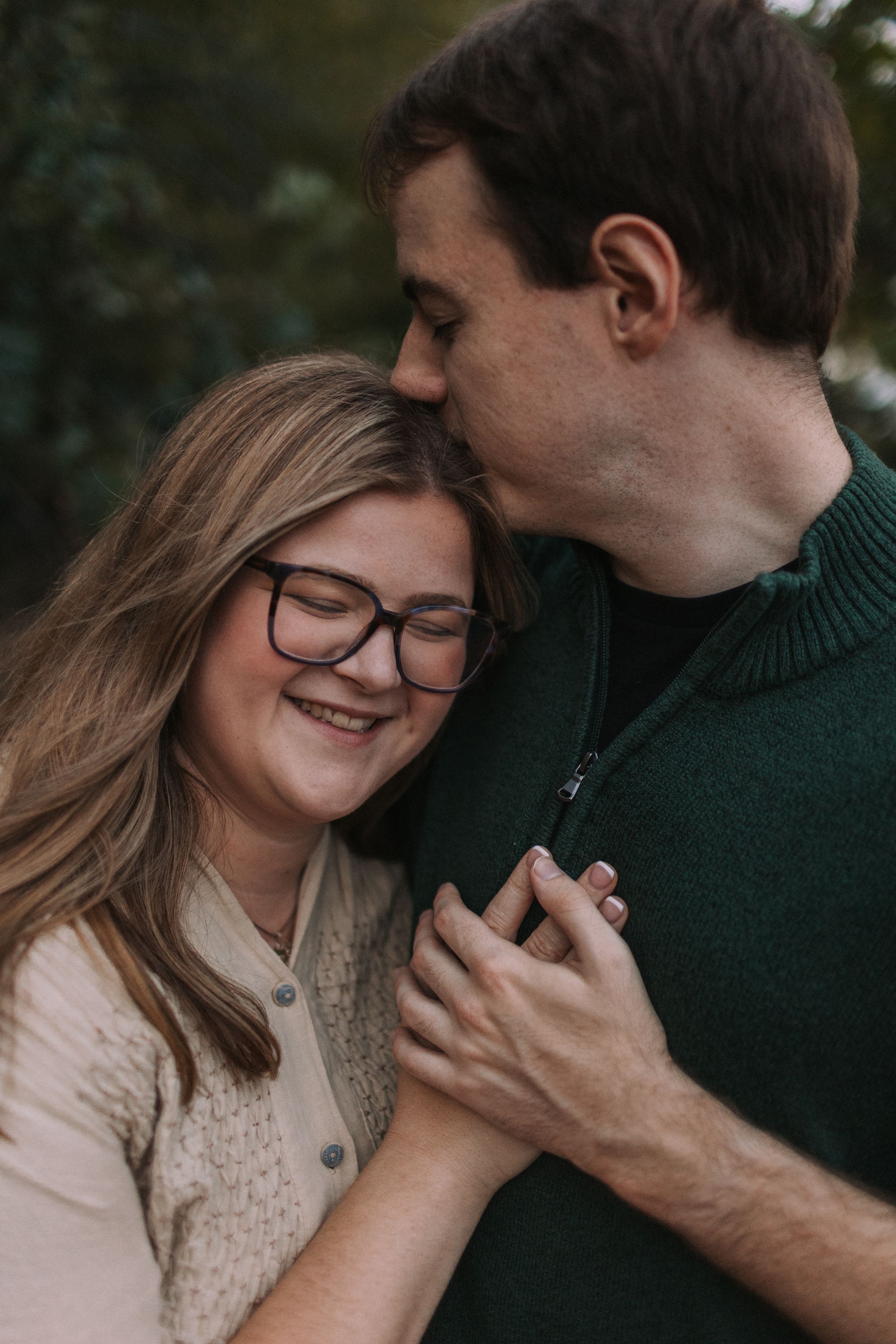 A romantic couple shares an intimate moment outdoors wearing cozy sweaters against a natural backdrop.