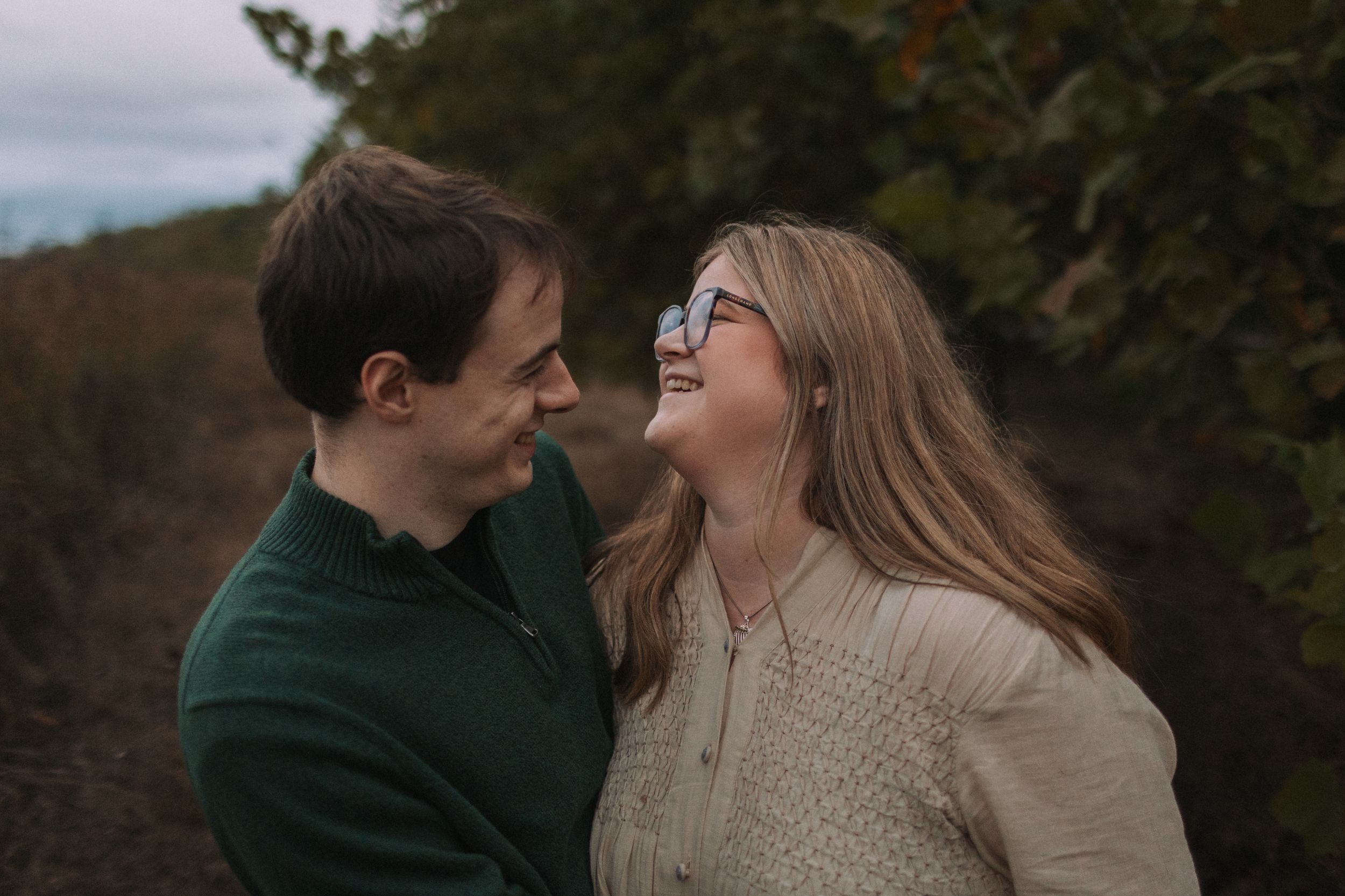 A couple shares a loving moment among autumn foliage wearing coordinating casual outfits.