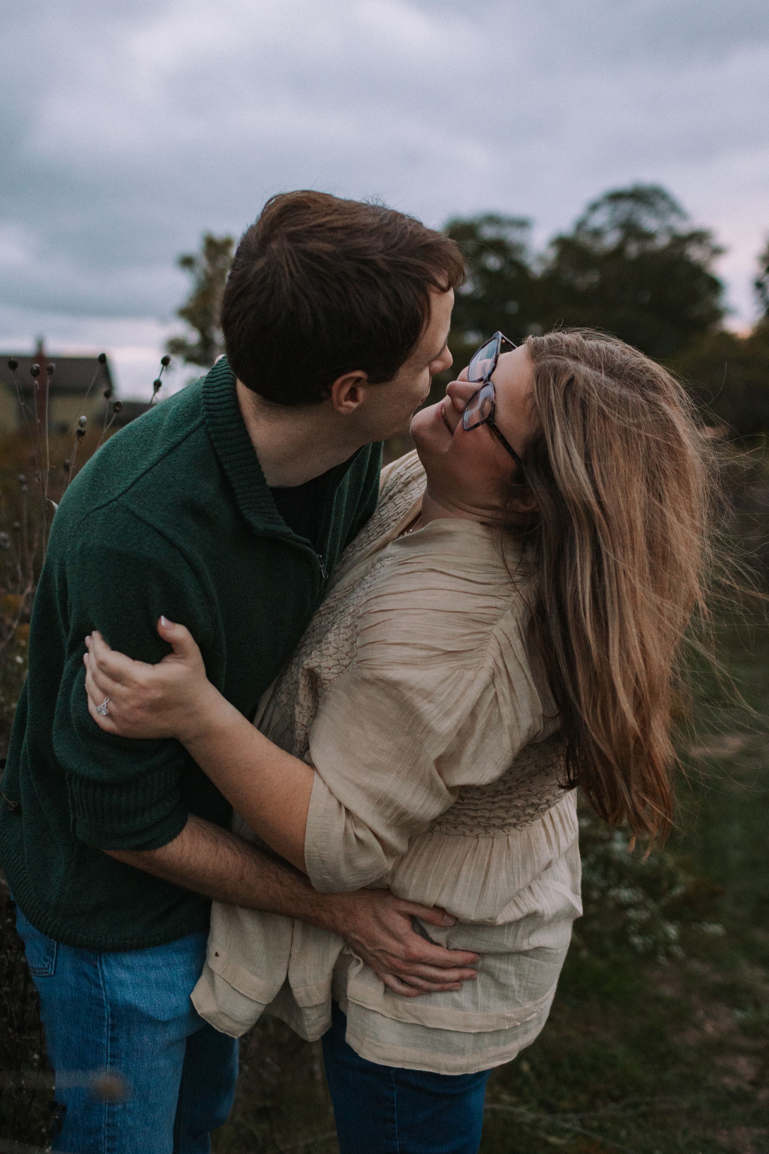 A couple shares laughter and embraces while standing in a rustic outdoor setting.
