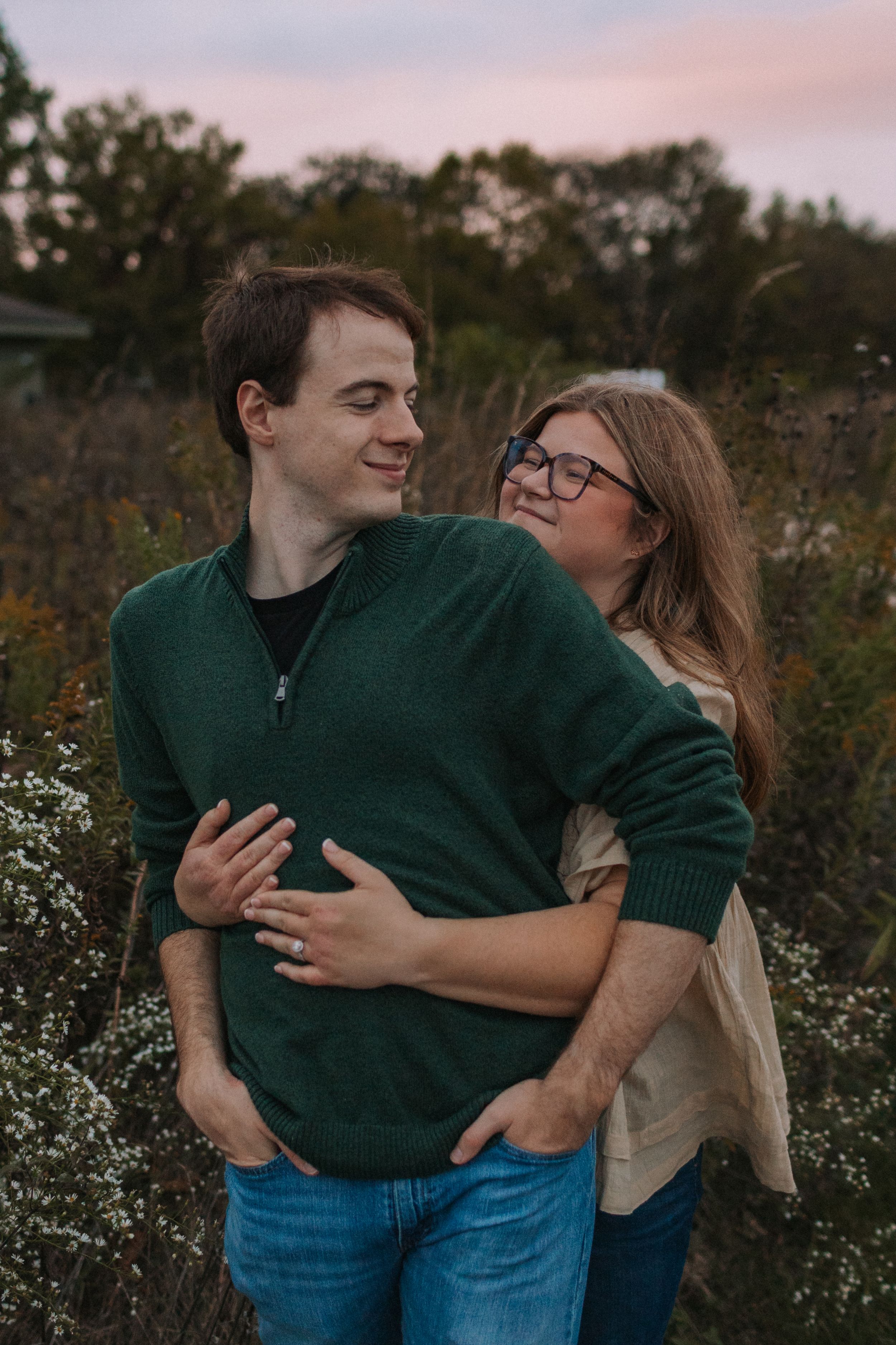 A couple laughs together while embracing in a field of wildflowers during golden hour.
