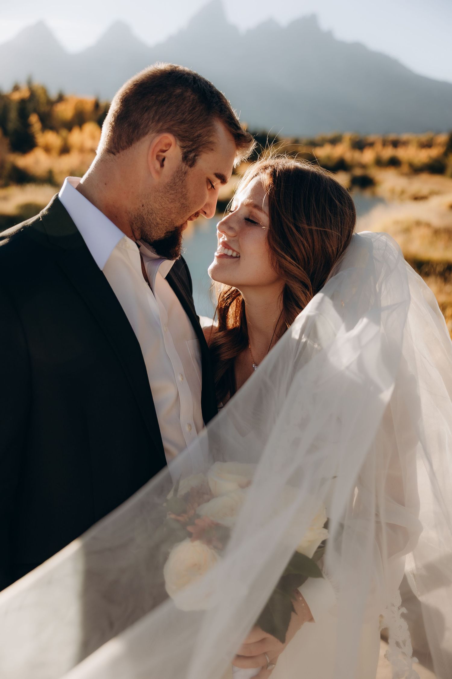 A romantic wedding photo with a flowing white veil against a mountain backdrop during golden hour.