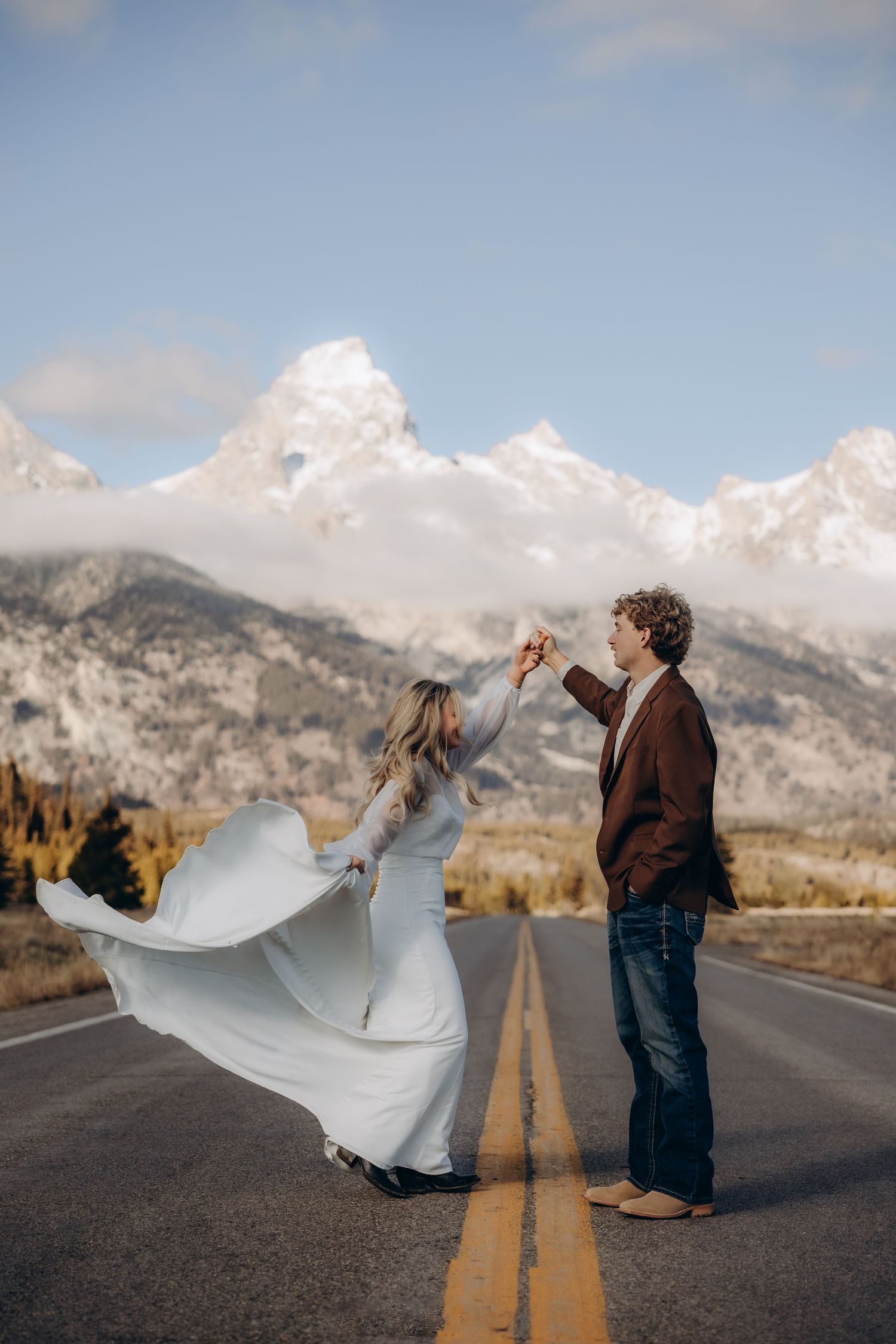 A rustic log cabin wedding ceremony with guests gathered against a dramatic mountain backdrop at sunset.