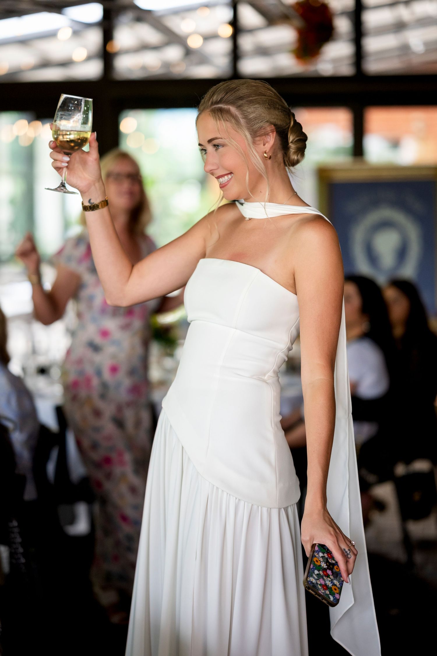 A sequence of photos showing someone in a flowing white dress holding a drink at an indoor reception venue.