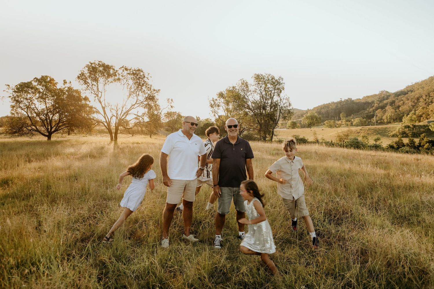 Family walking together through a golden grass field at sunset on a warm summer evening.