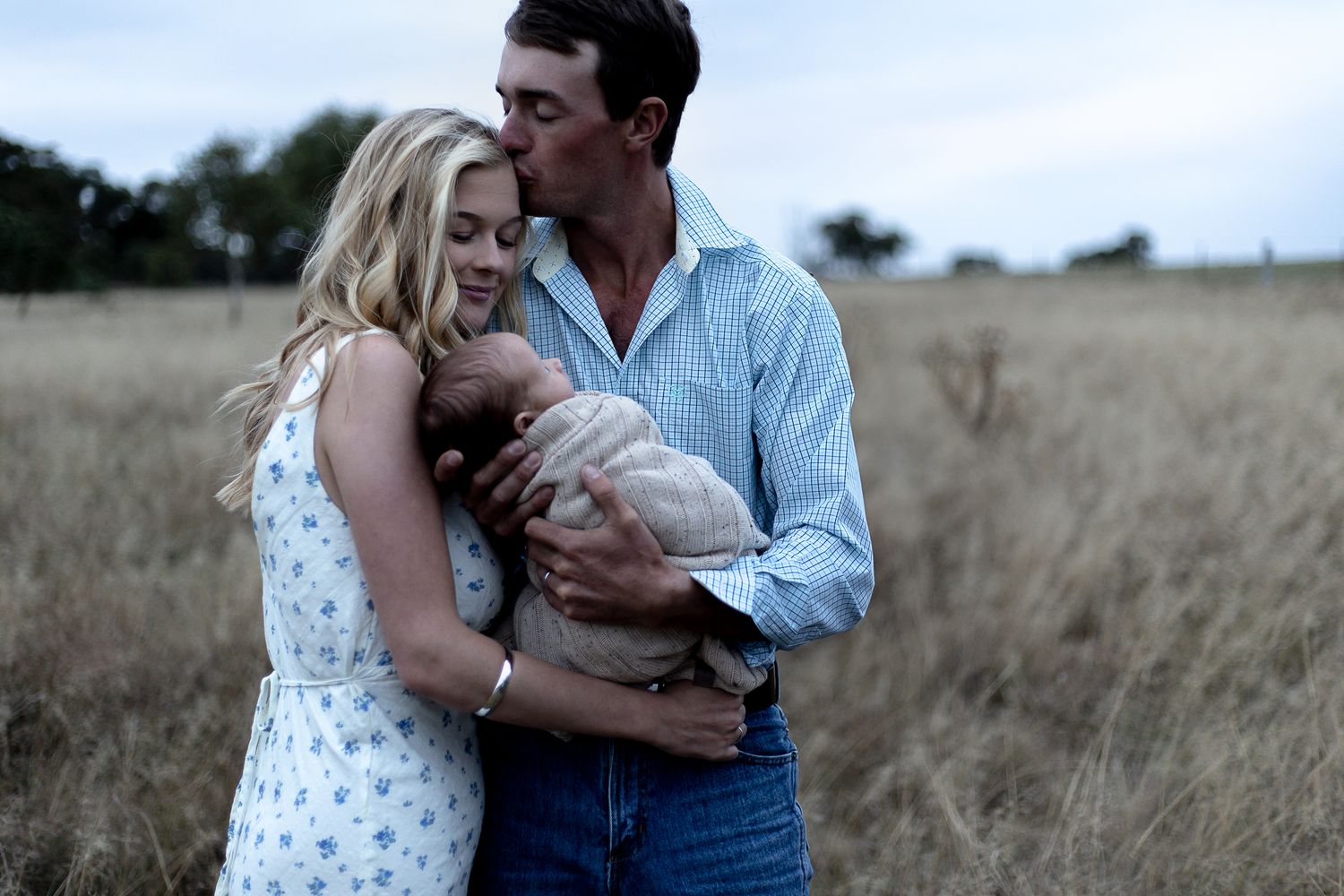 Father kissing mother while holding their newborn baby during a professional newborn photo shoot.