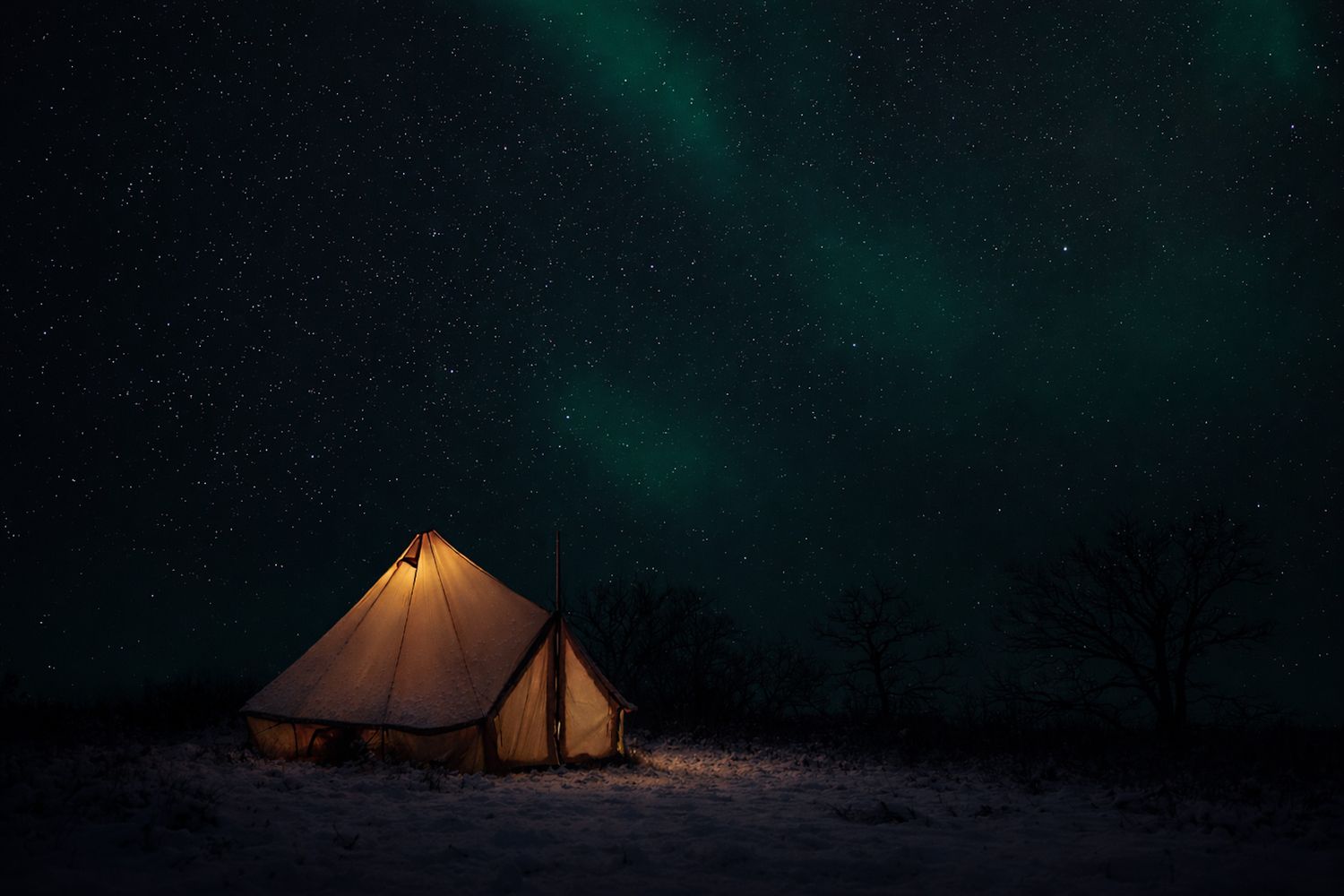Orange tent glows under dramatic green northern lights display in dark night sky.