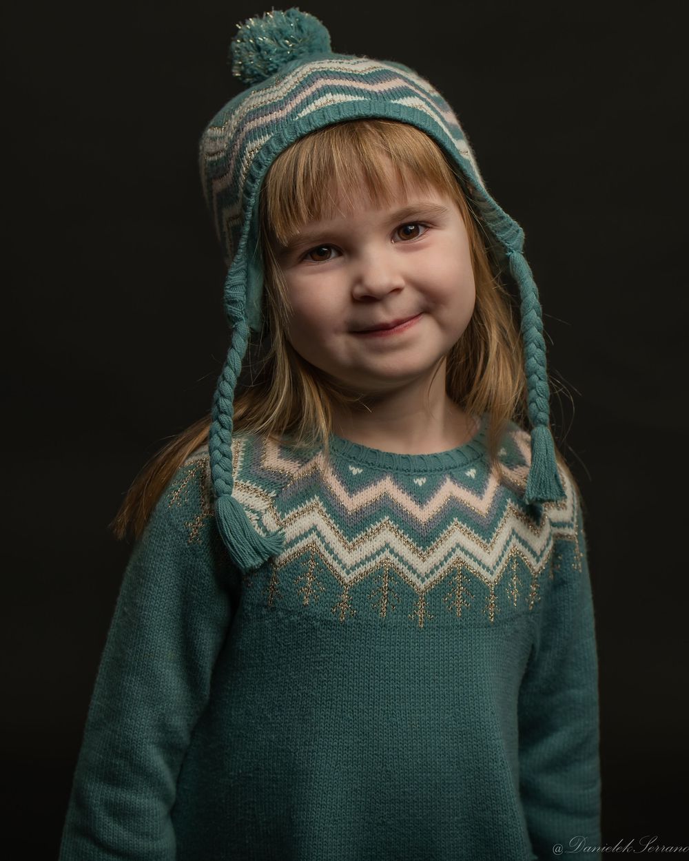 Smiling child in teal zigzag knit sweater and matching earflap hat portrait.