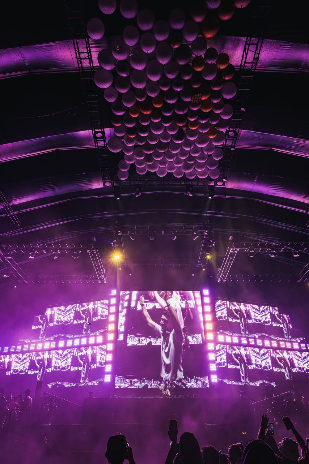 Concert stage with purple lighting and hanging spherical decorations creates an immersive electronic music atmosphere.
