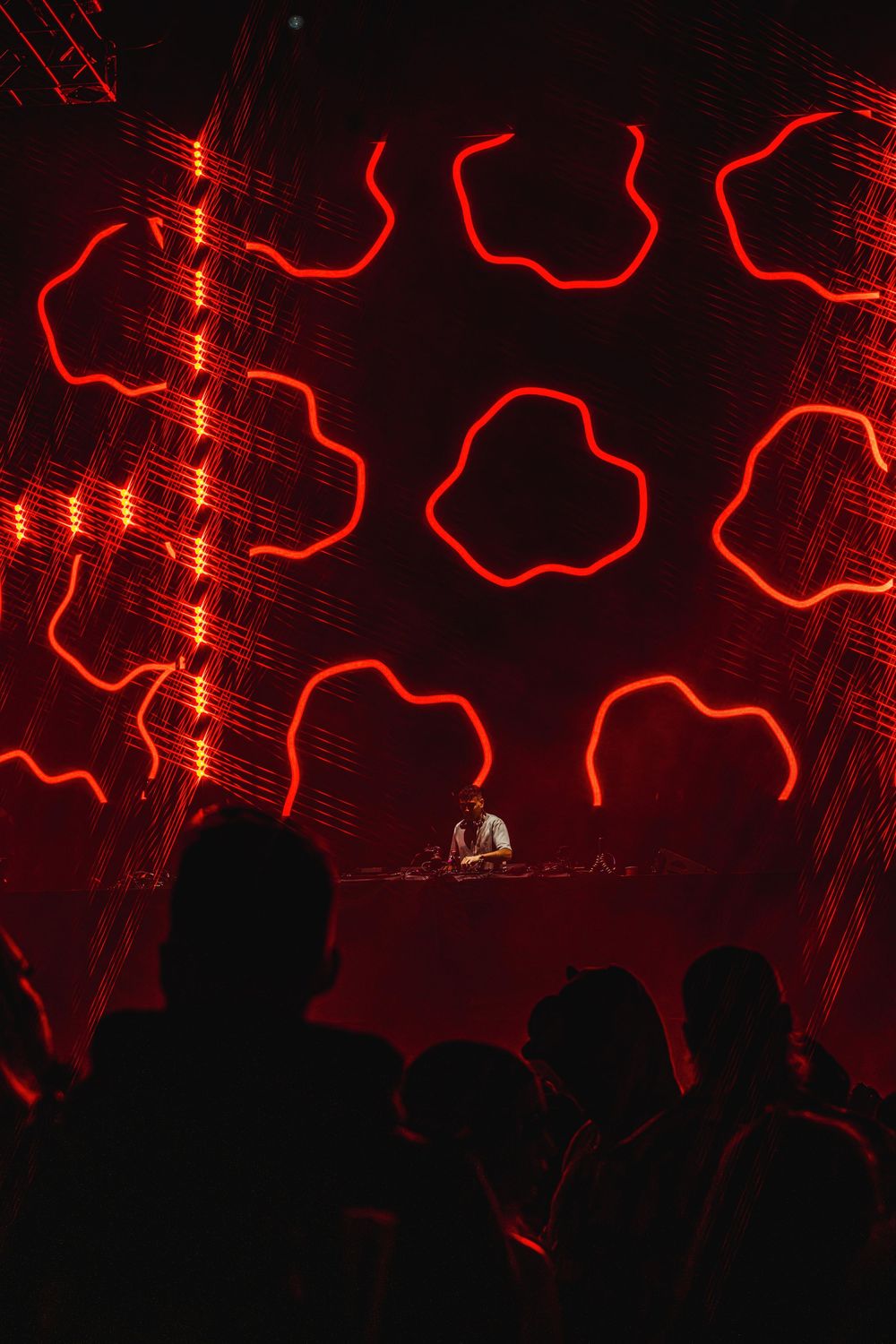 Silhouettes of concert crowd against dramatic red lighting and wavy patterns on stage display.