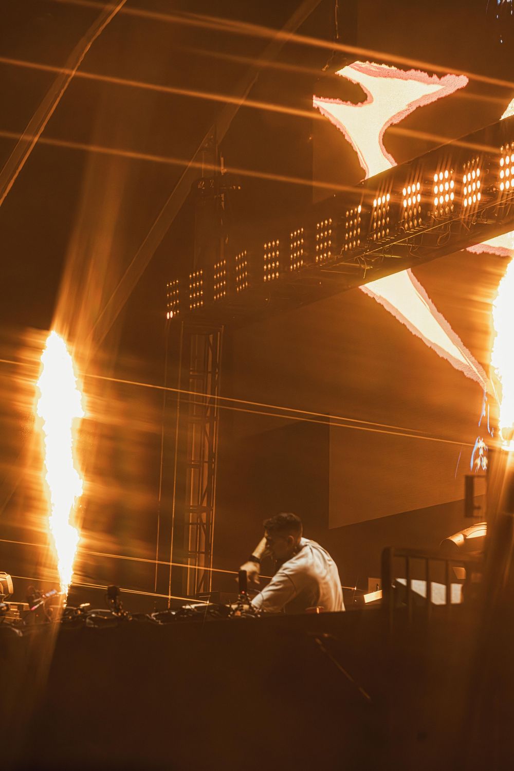 Silhouetted figures perform on stage with dramatic orange lighting and smoke effects creating a moody atmosphere.
