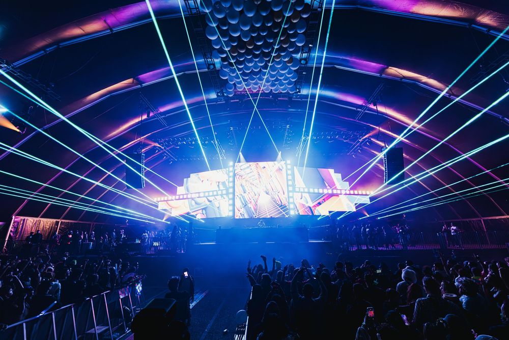 Concert arena with vibrant blue and purple lighting effects illuminating the stage and crowd during a live performance.