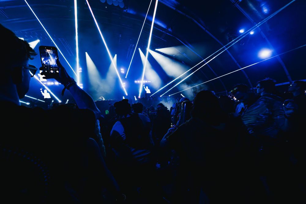 Concert crowd illuminated by bright blue stage lights and spotlights during a live performance.