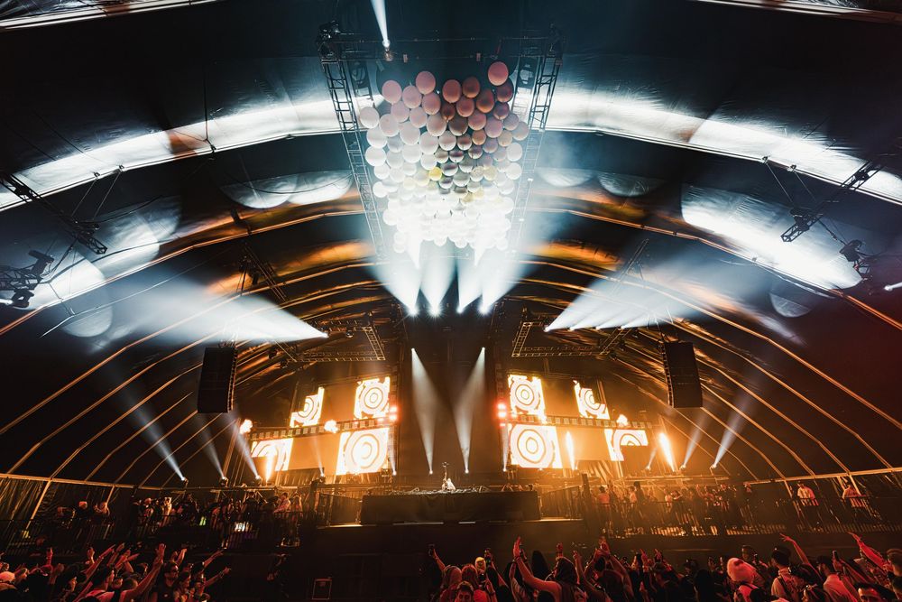 Concert venue filled with colorful lights and lasers illuminating a massive crowd during an electronic music performance.