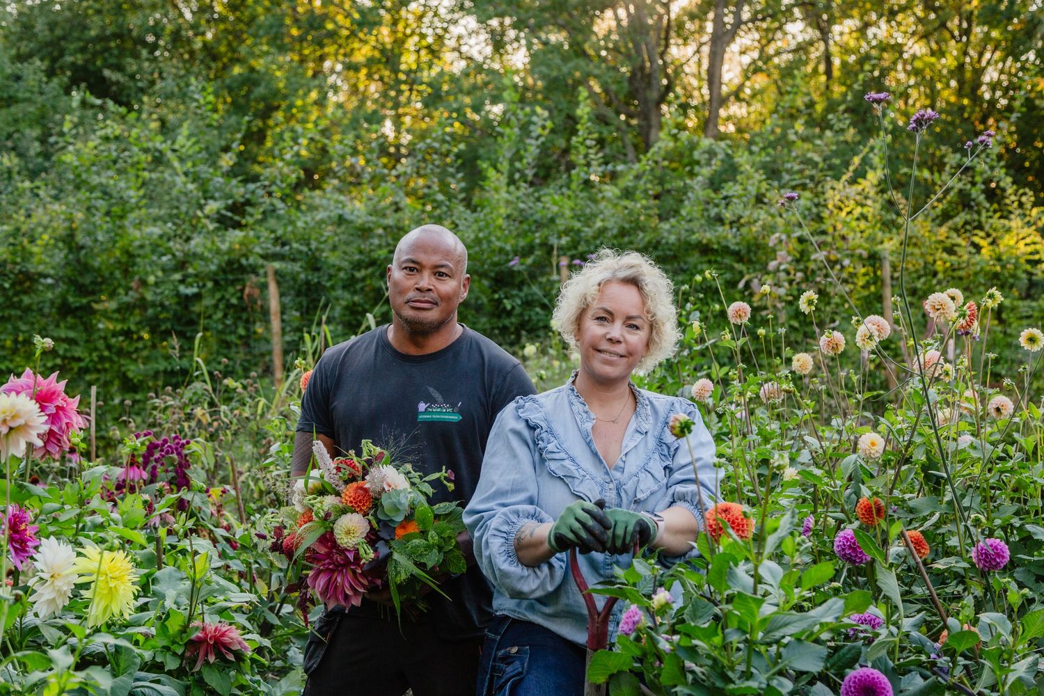 Two people holding freshly harvested flowers in blooming garden at sunset.
