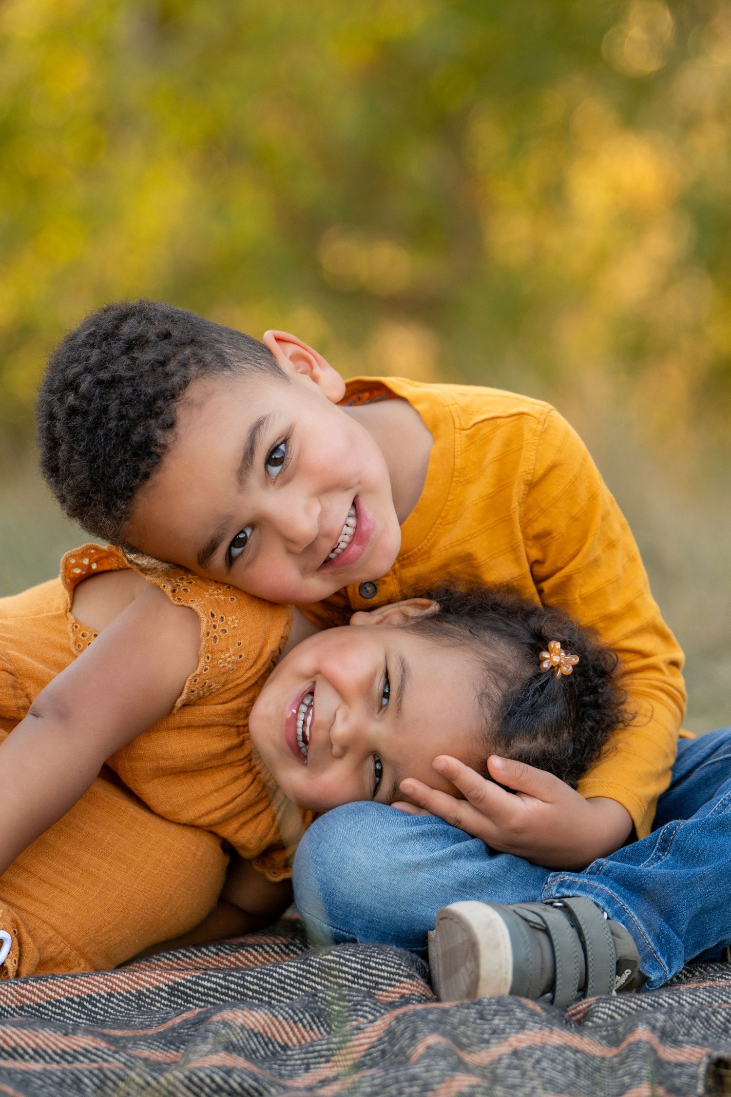Two children in autumn colors share a tender playful moment on a blanket outdoors.
