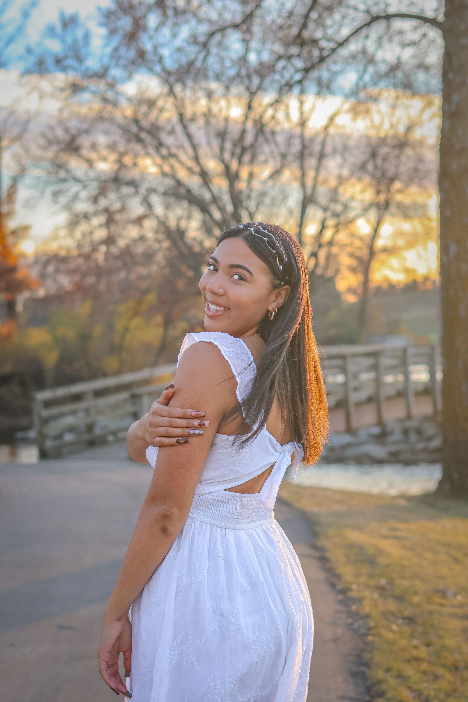 Woman in white dress smiling over shoulder on bridge during sunset.
