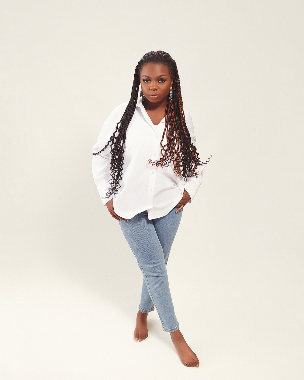Someone wearing a crisp white button-down shirt and light blue jeans poses barefoot against a neutral background.