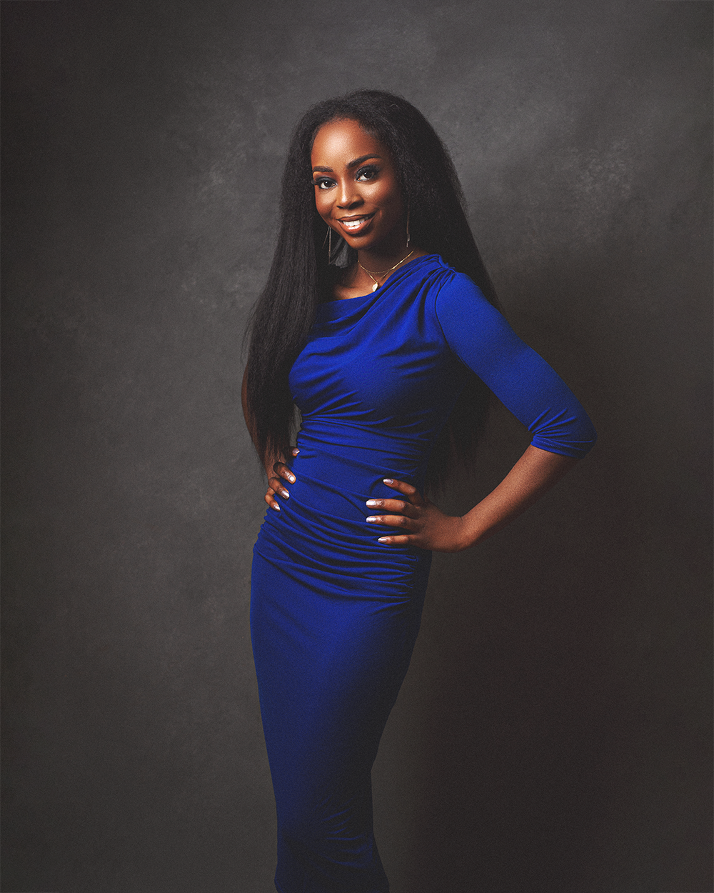 A woman in a fitted royal blue dress poses confidently against a dark backdrop during a studio photoshoot.