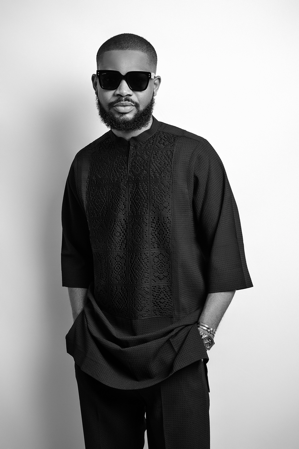 A black and white portrait in traditional African attire and sunglasses.