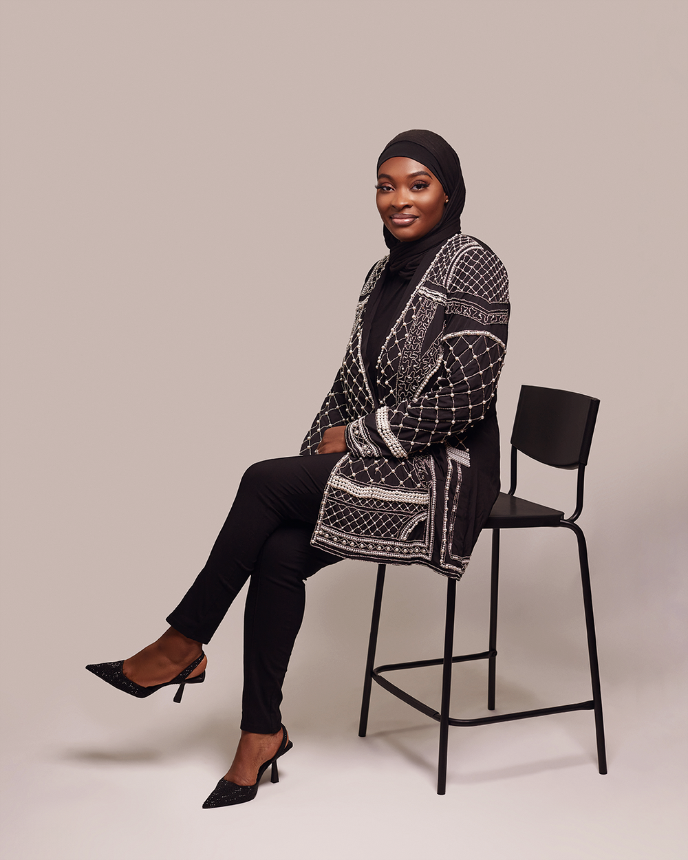 Stylish black and white patterned cardigan paired with dark pants and heels against a neutral studio backdrop.