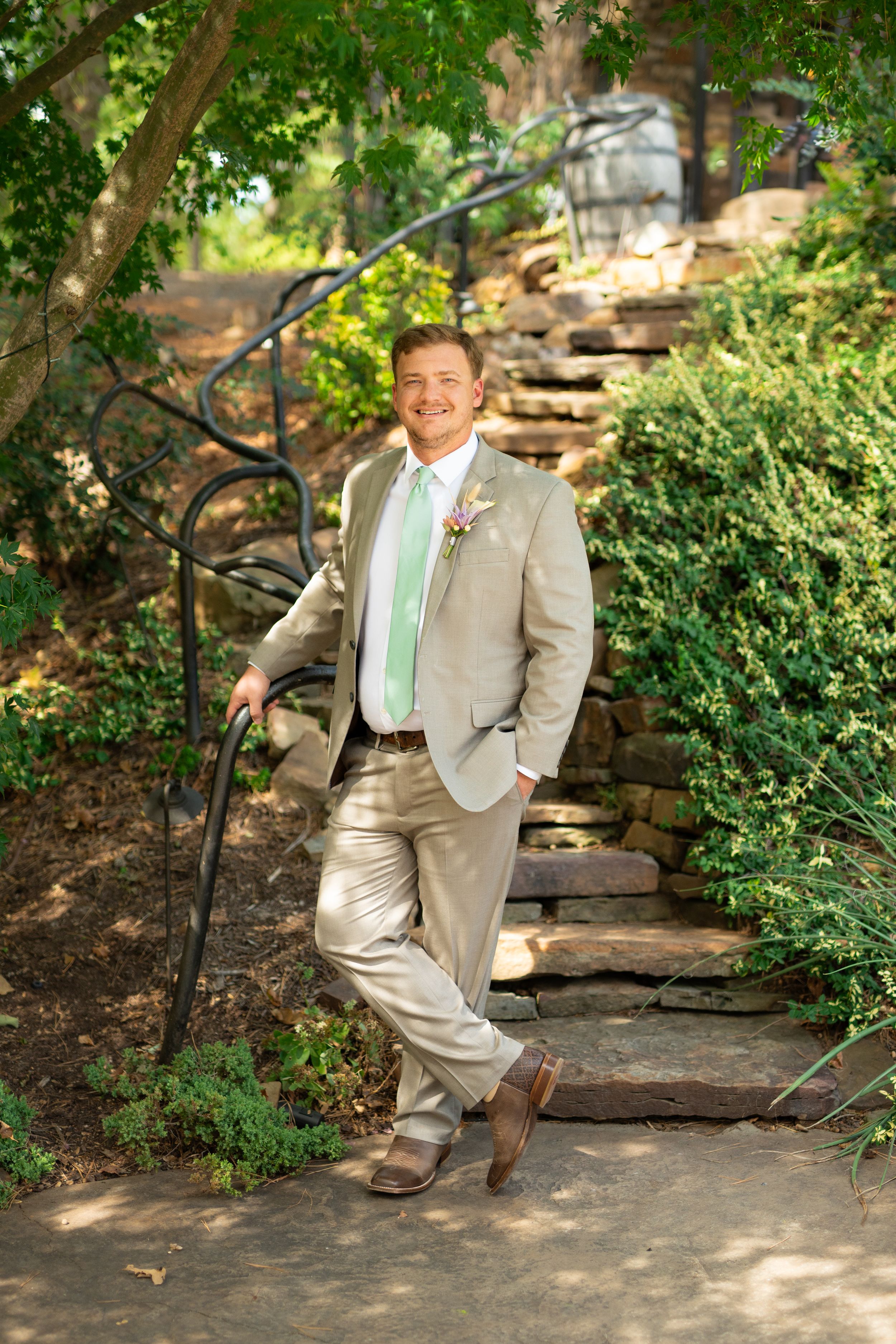 Person in light tan suit strikes playful poses on stone path surrounded by lush greenery.