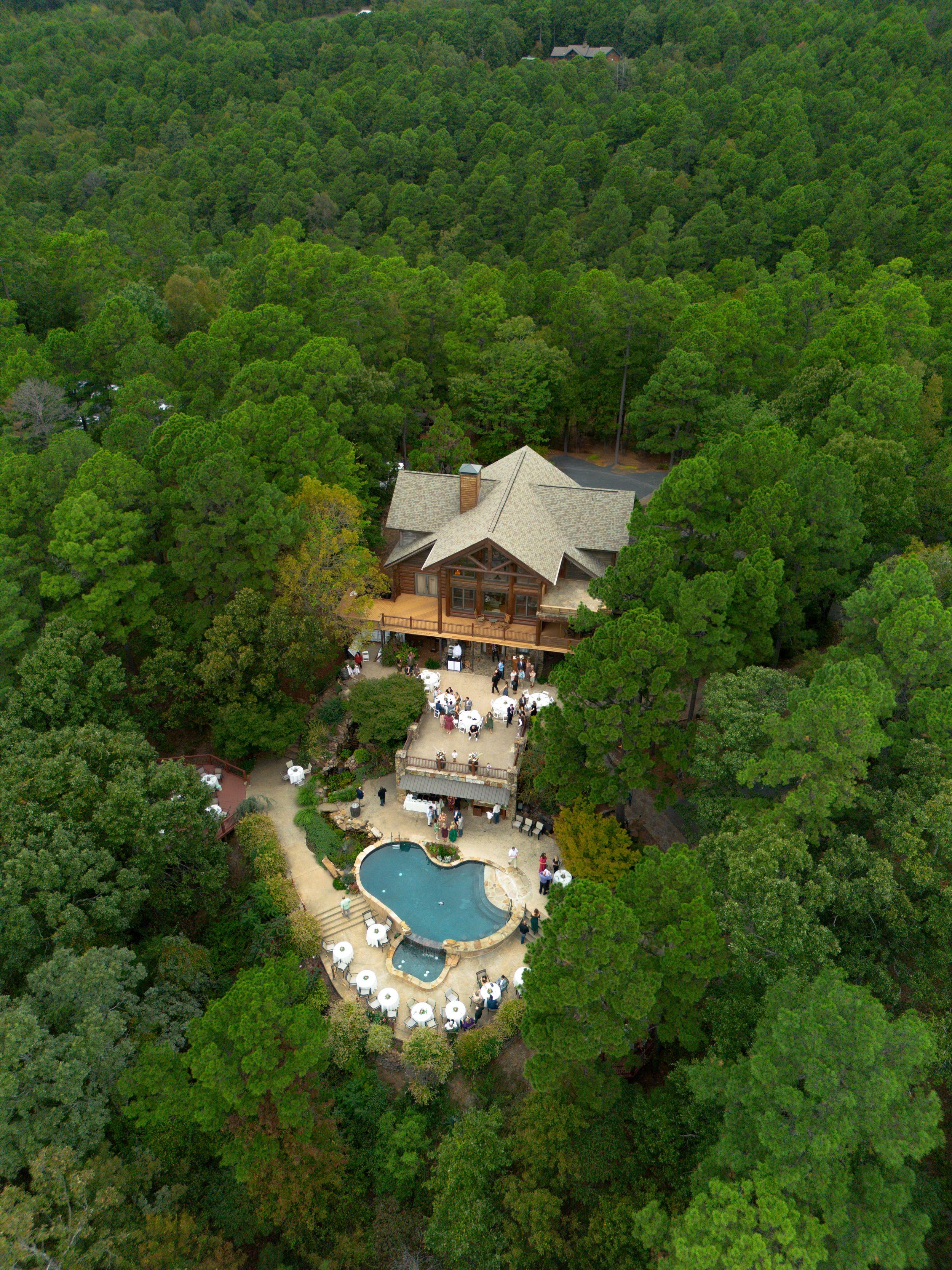 Aerial view of venue surrounded by dense forest with outdoor pool and event setup.