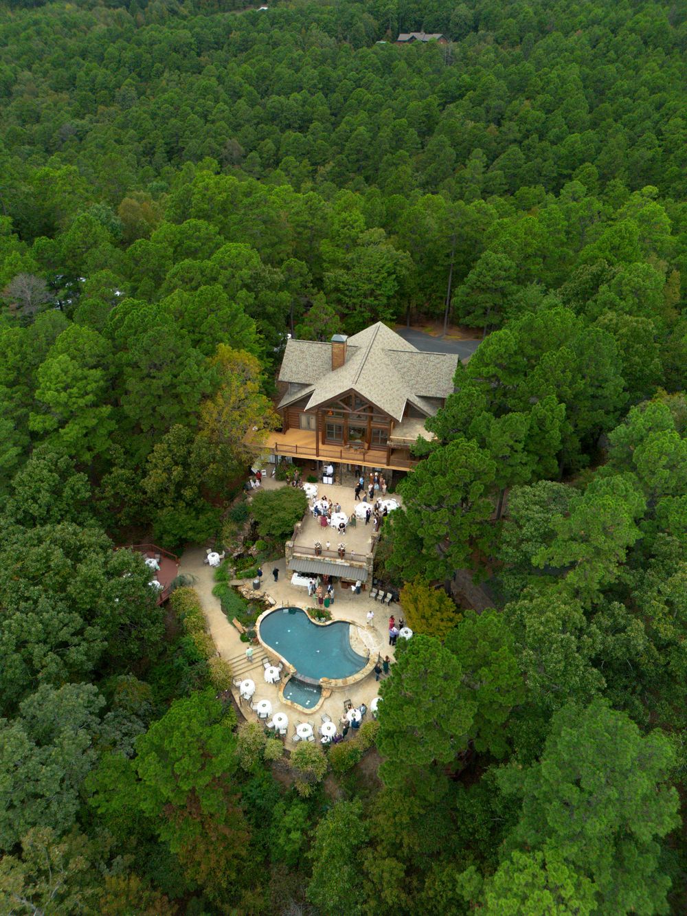 Aerial view of venue surrounded by dense forest with outdoor pool and event setup.