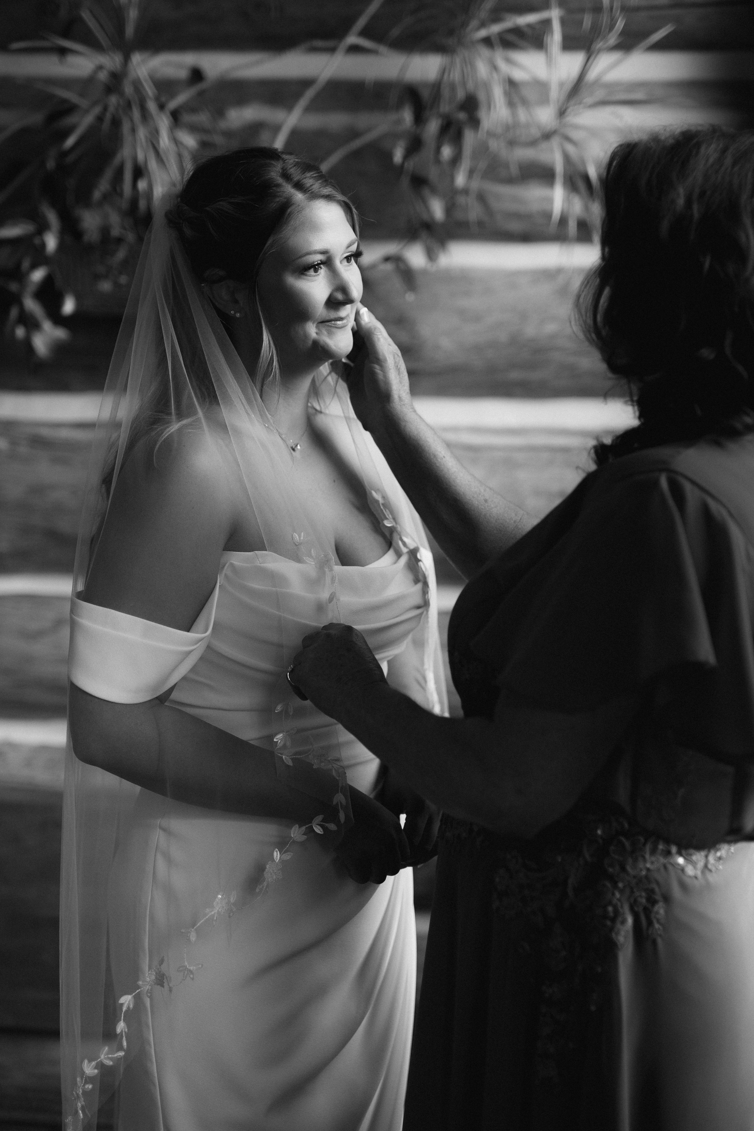 Black and white image of bride getting help with wedding dress preparations.