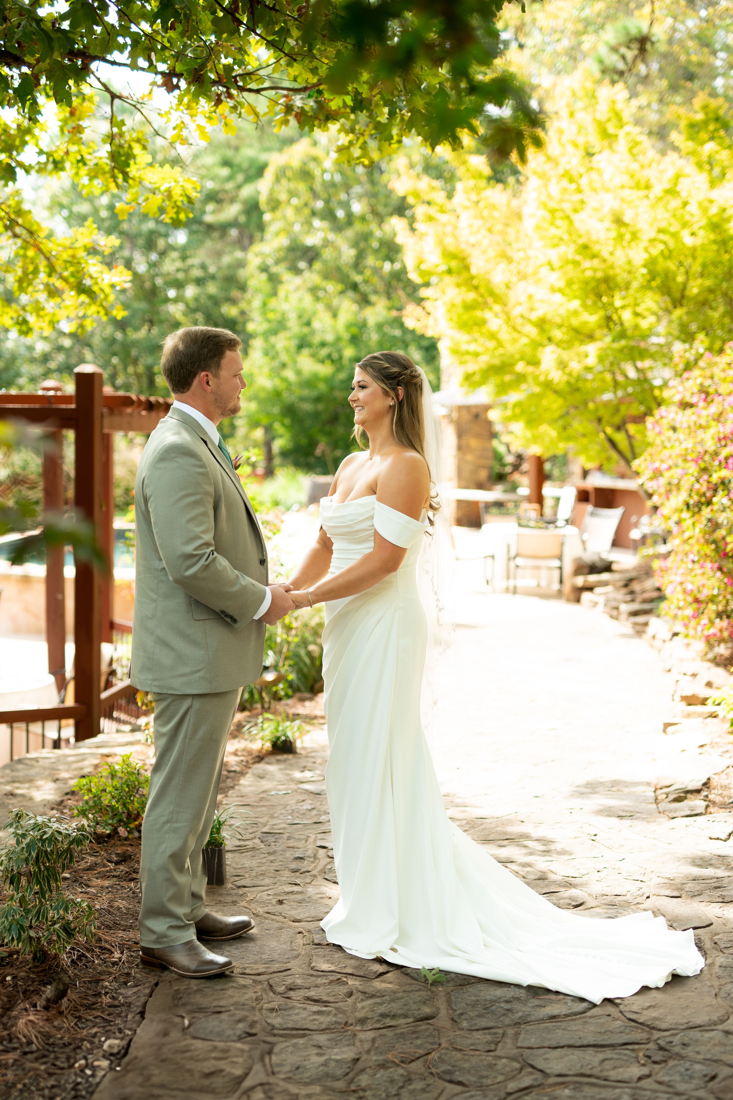 Bride and groom dance playfully on a stone pathway surrounded by sunlit trees.