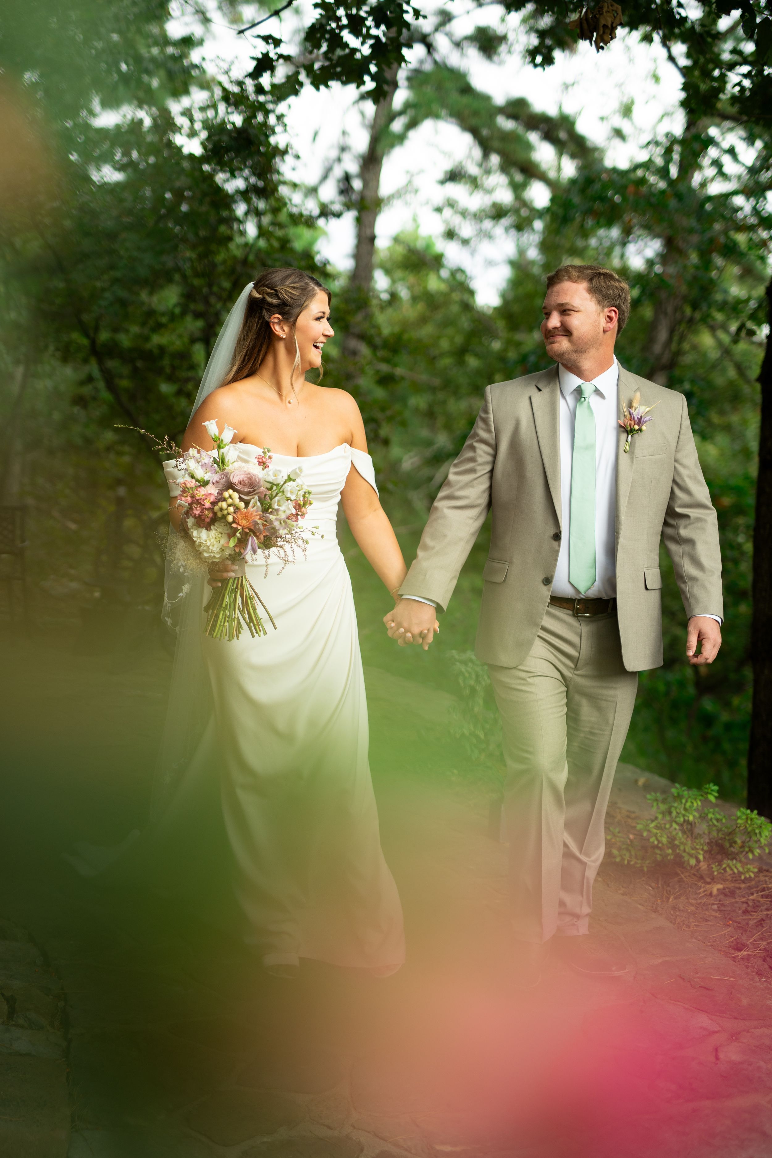 A wedding couple shares a romantic moment outdoors, with the bride in white and groom in gray suit with mint tie.