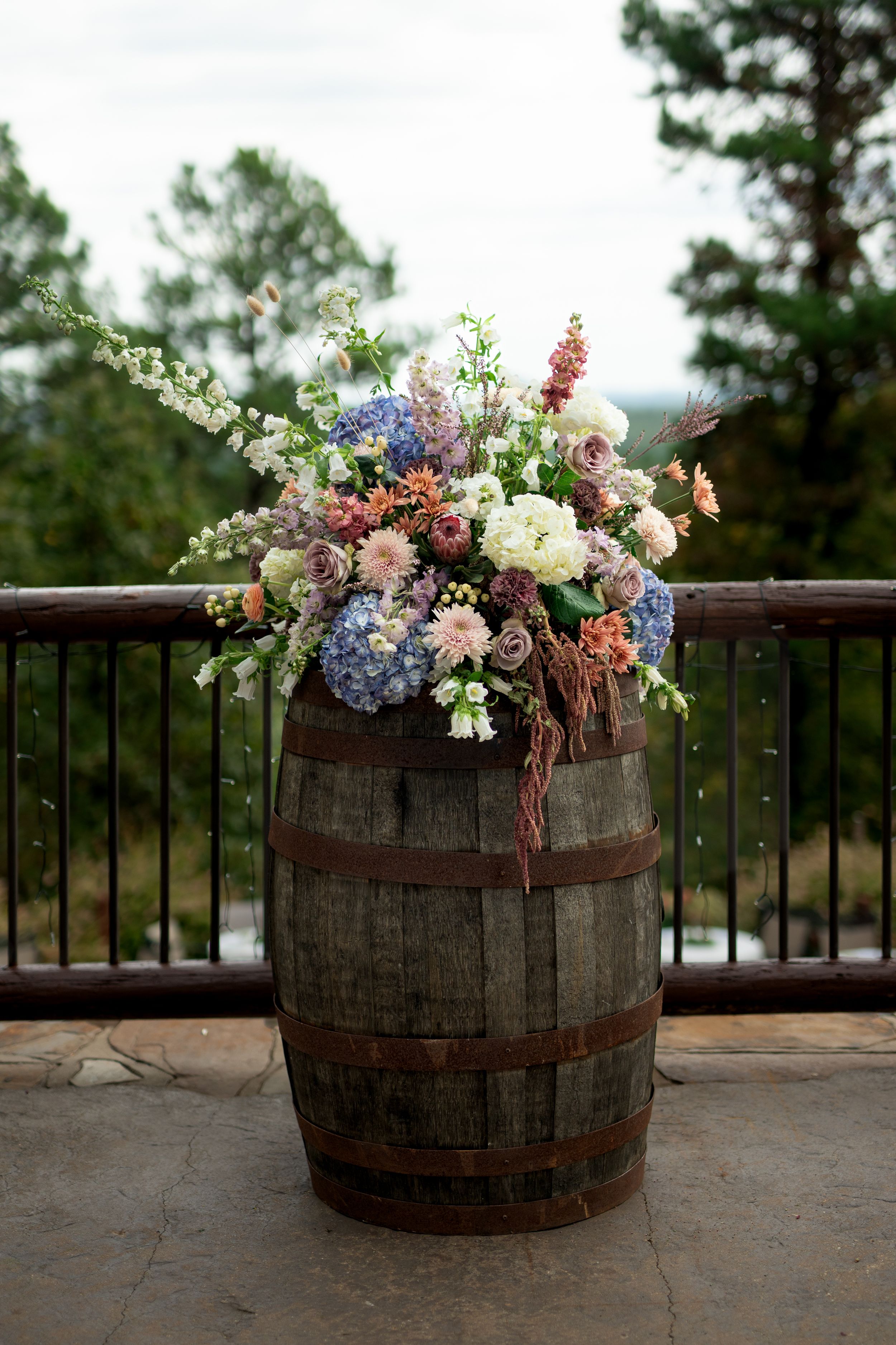 Rustic wine barrel decorated with elegant floral arrangements featuring pink, blue and white blooms.