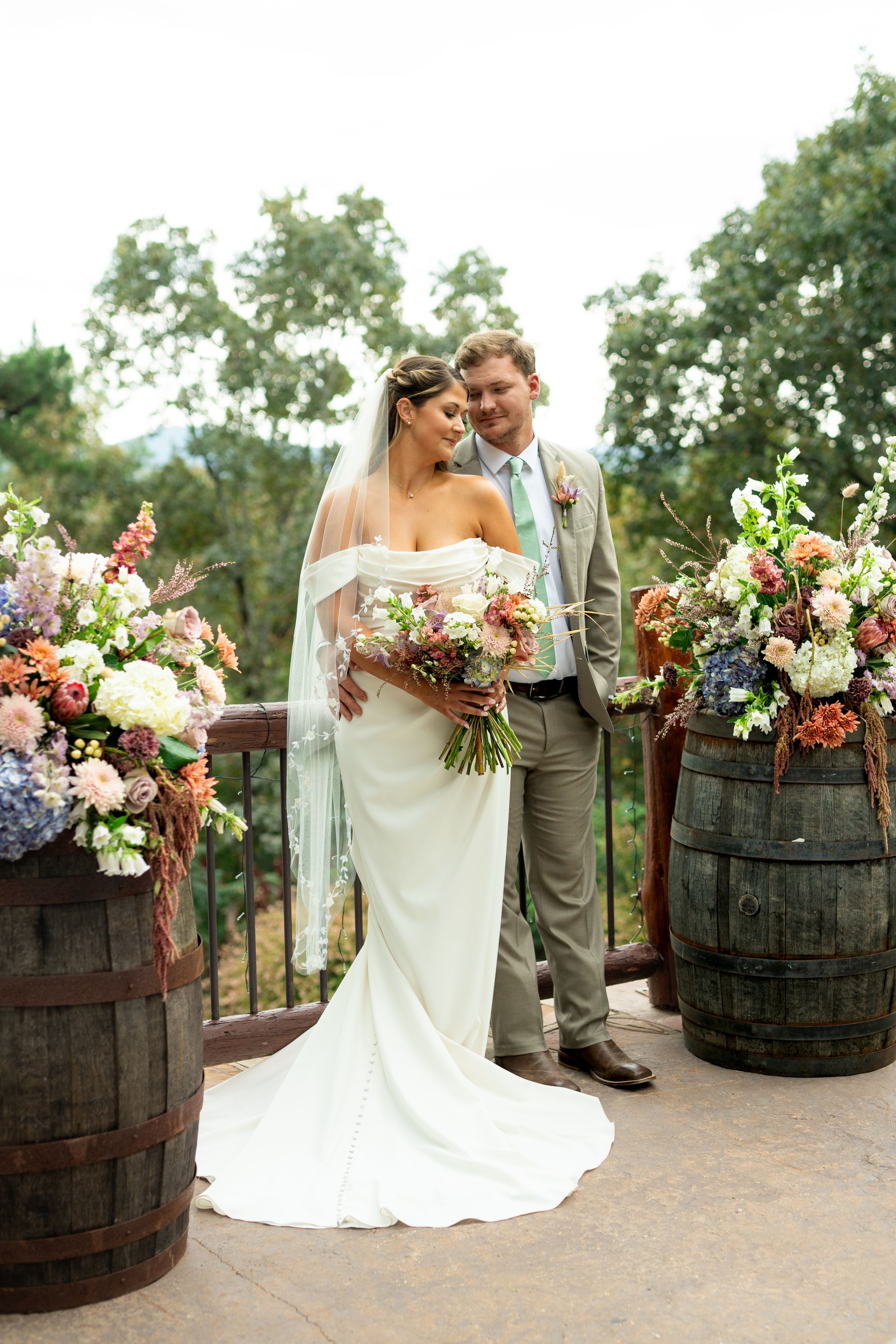 Outdoor wedding scene with decorative wine barrels and floral arrangements on a stone patio.