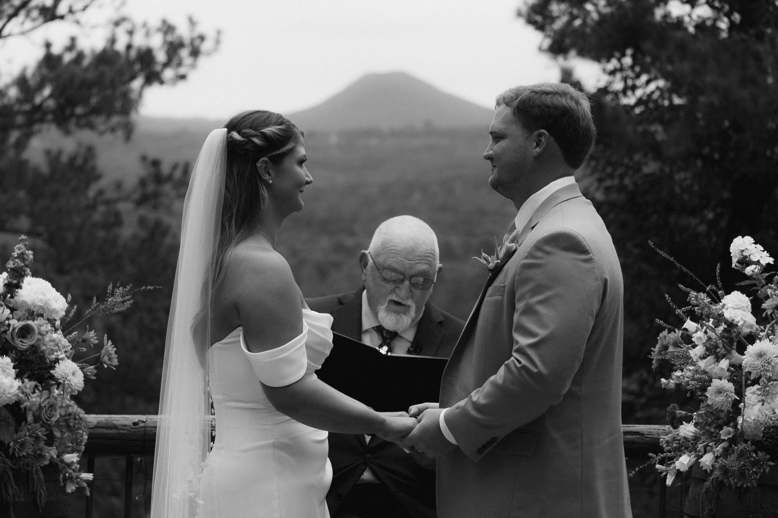 Outdoor wedding ceremony scene with mountain backdrop and white floral decorations.