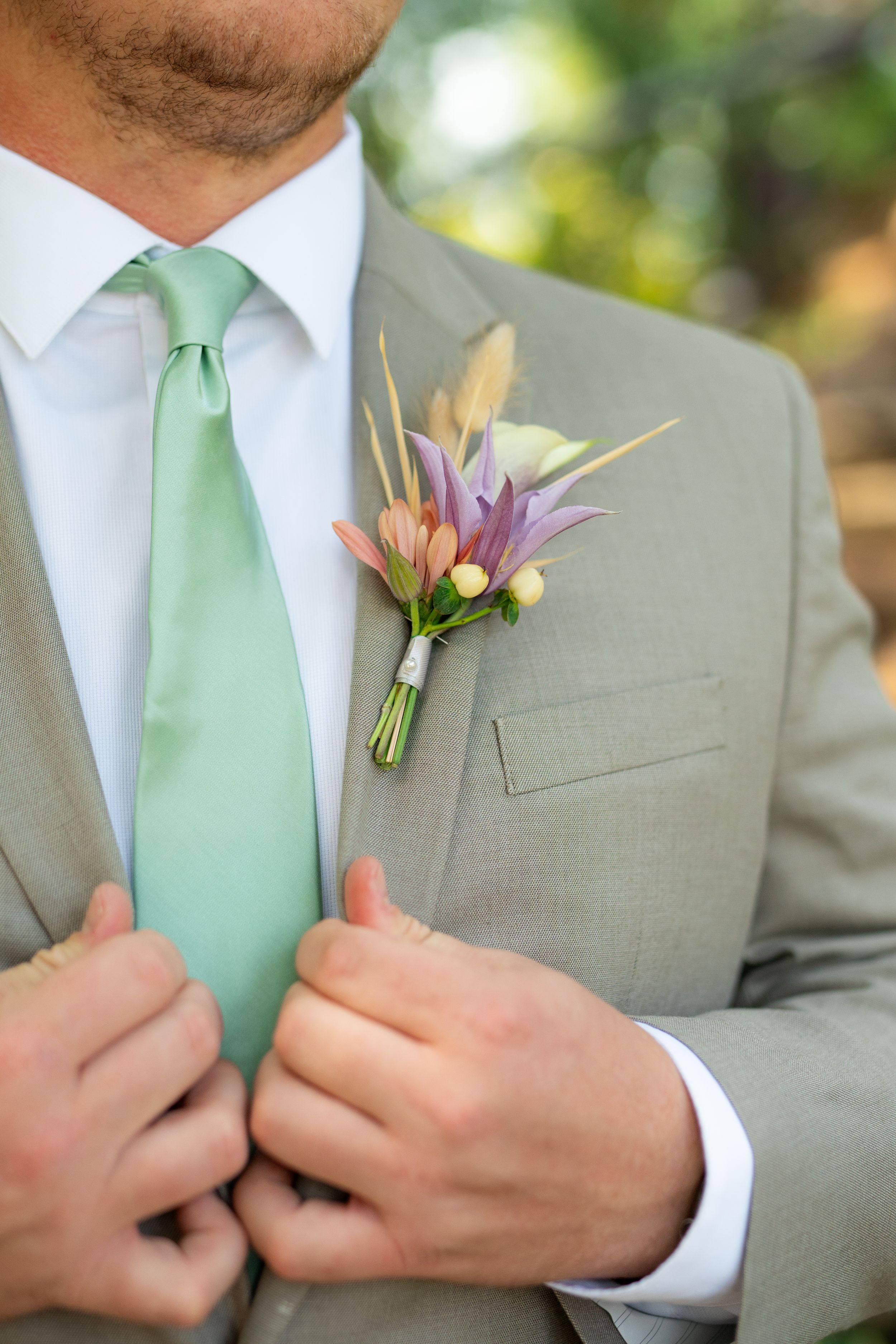 Close up of groom's gray suit with mint green tie and pink boutonniere.