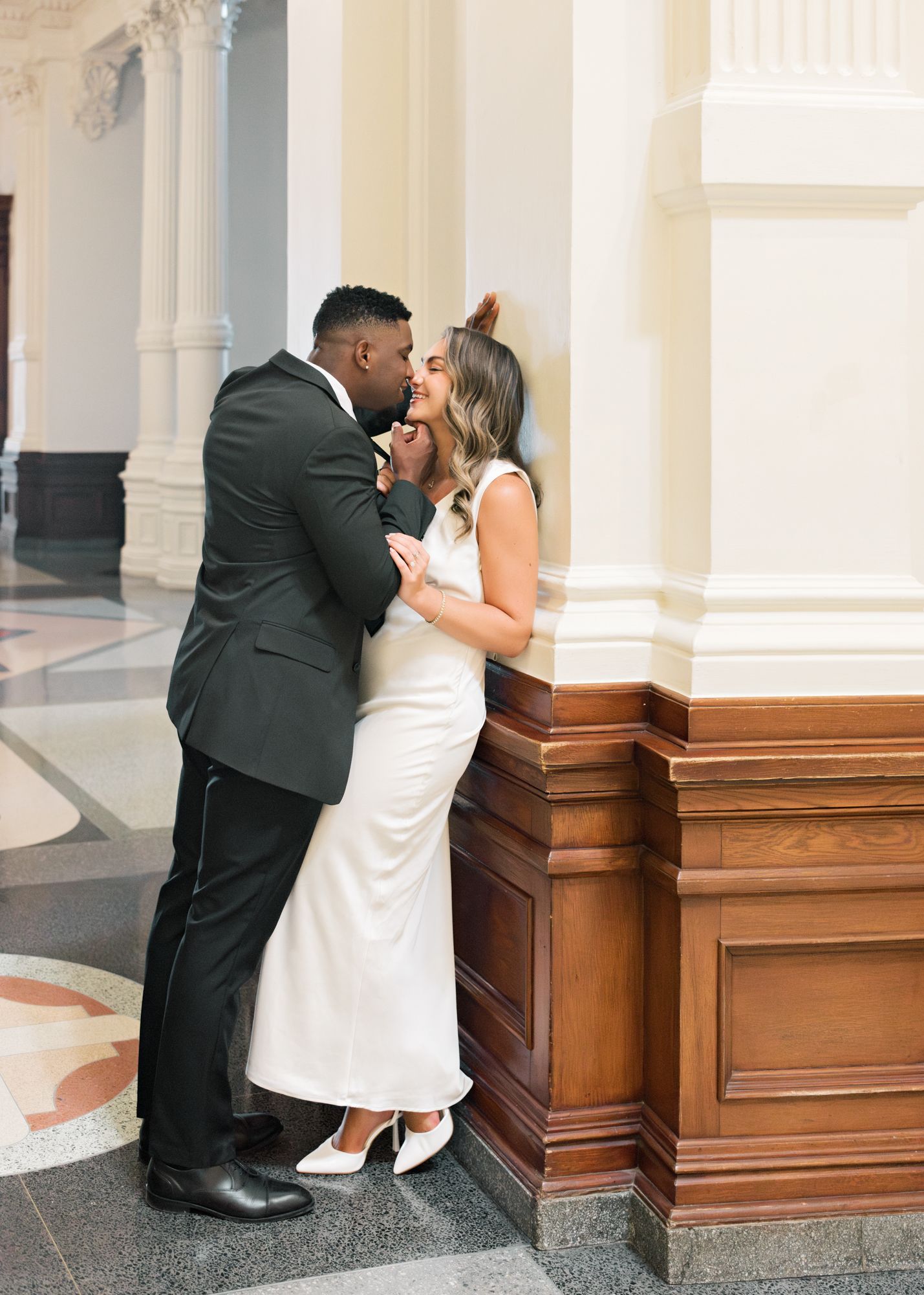A romantic moment captured in a grand hallway with white columns and marble floors.