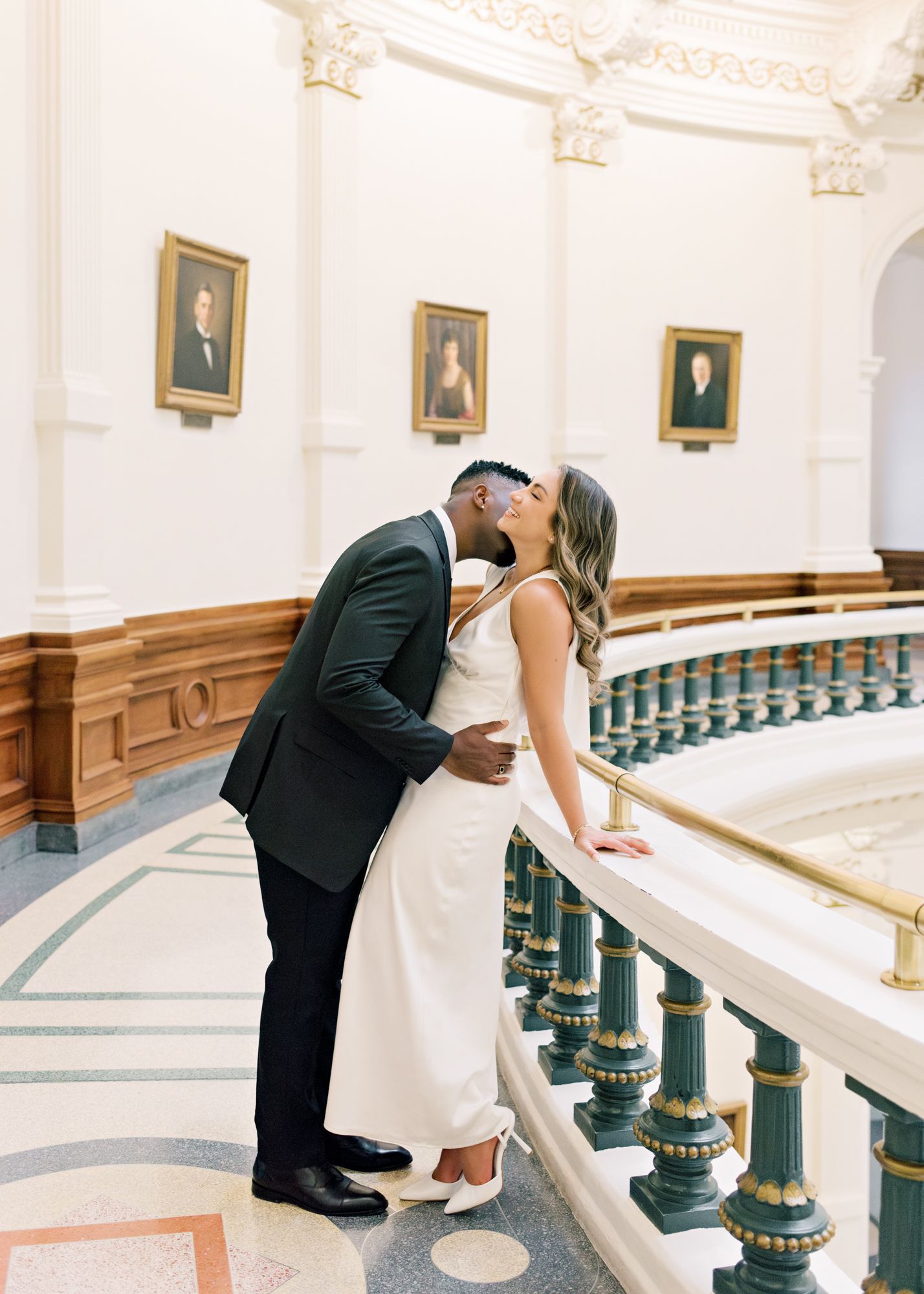 A romantic kiss shared along an ornate railing in a historic building.