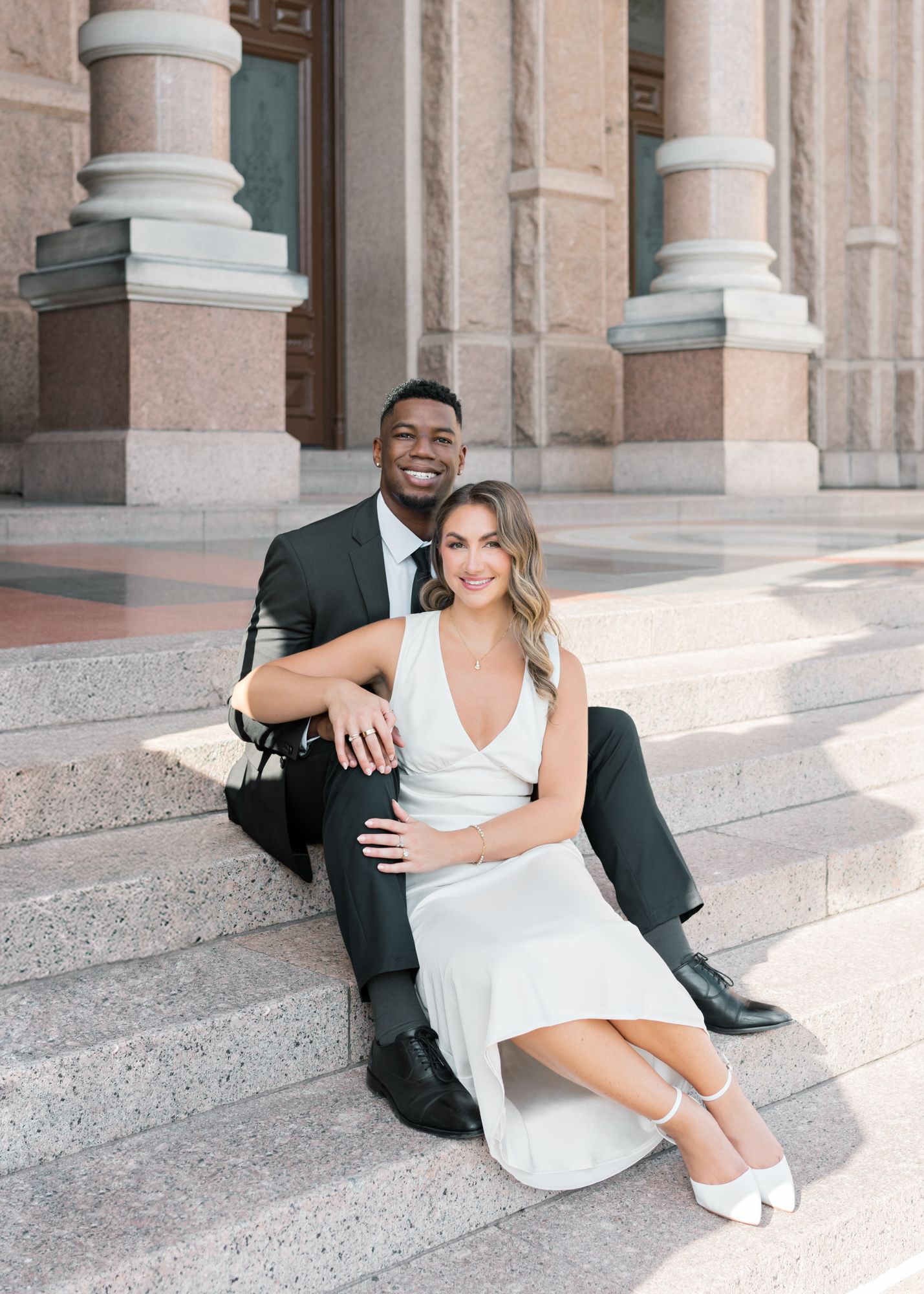 A couple posing on stone steps in formal attire outside a classical building with columns.