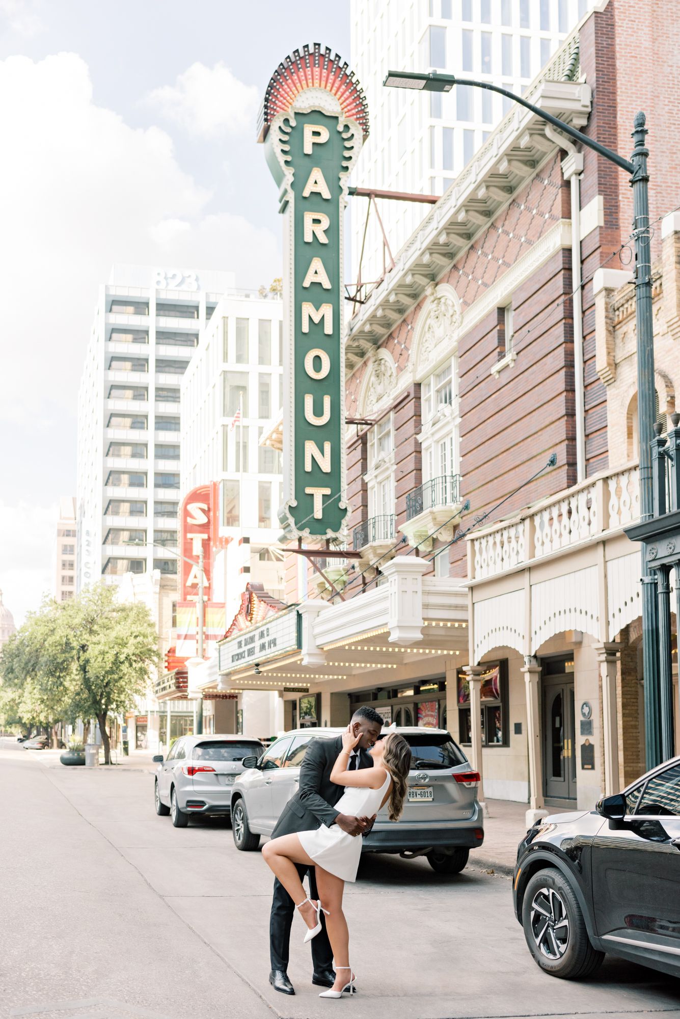 A couple embracing under the vintage Paramount theater sign in an urban setting.