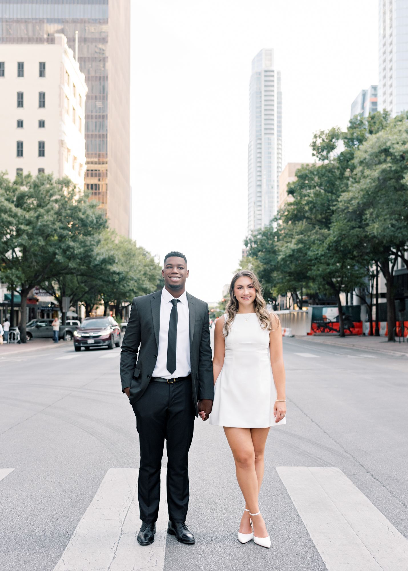 A couple walking together on an urban street with modern buildings and trees in downtown.