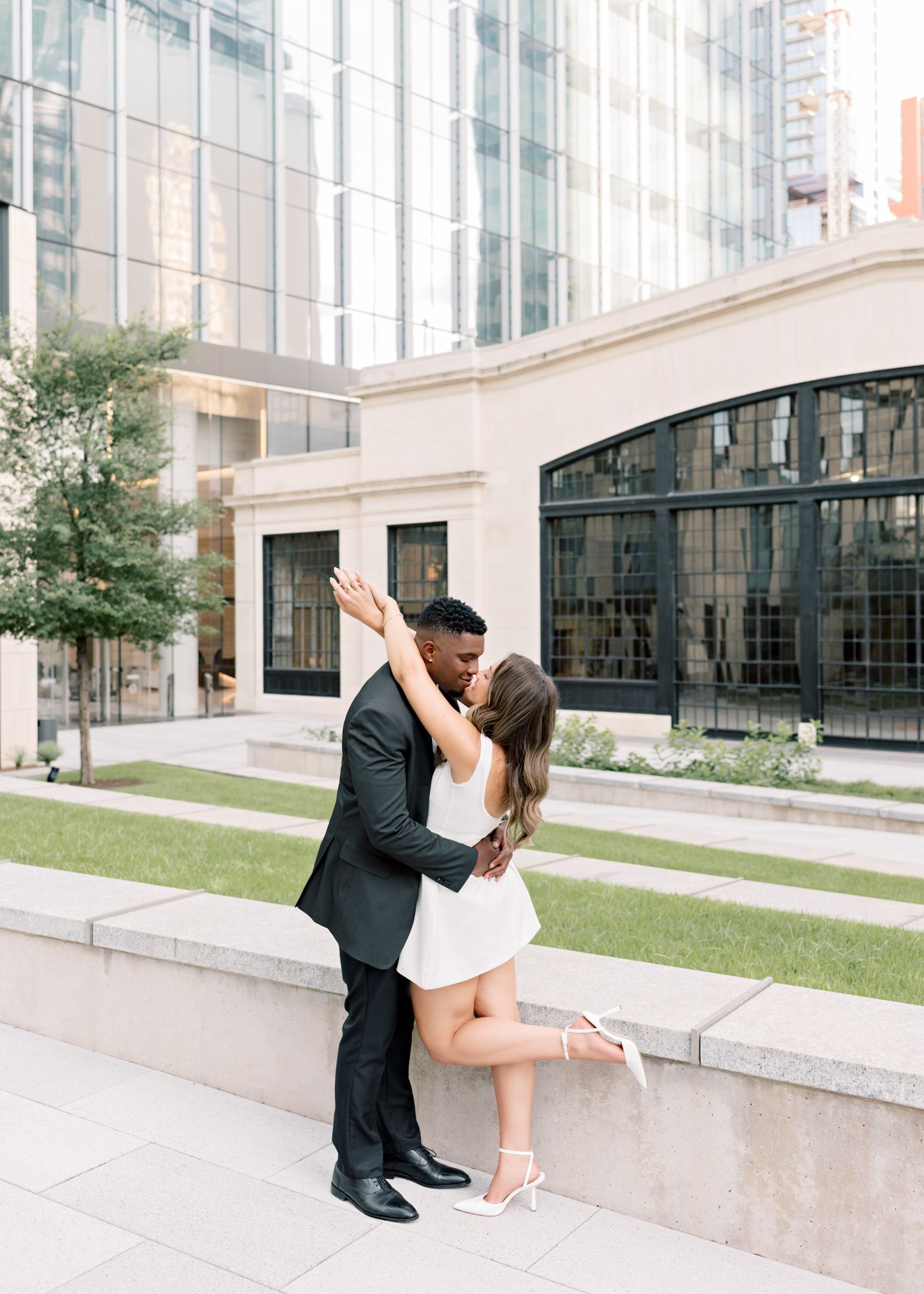A romantic dance pose between a couple in formal wear outside a modern building.