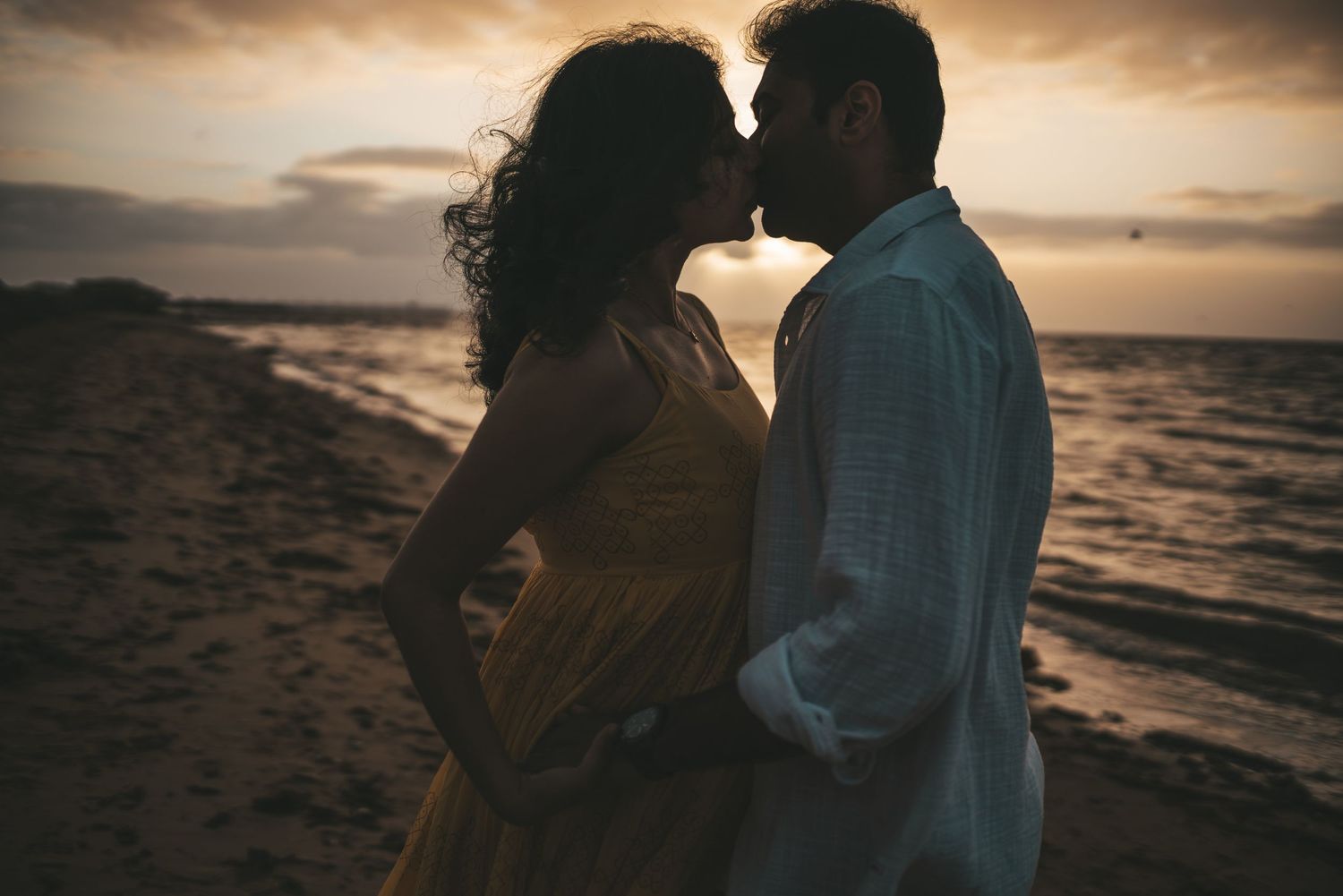 Romantic silhouette of couple sharing intimate moment at beach during golden sunrise taken by Melbourne maternity photographer.