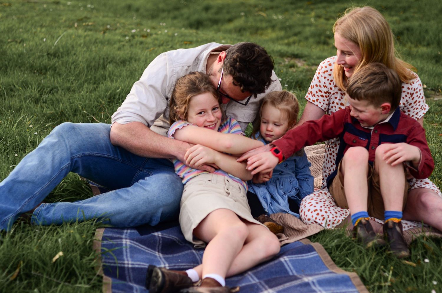 Family having a picnic together on a blanket in green grass on a sunny day.