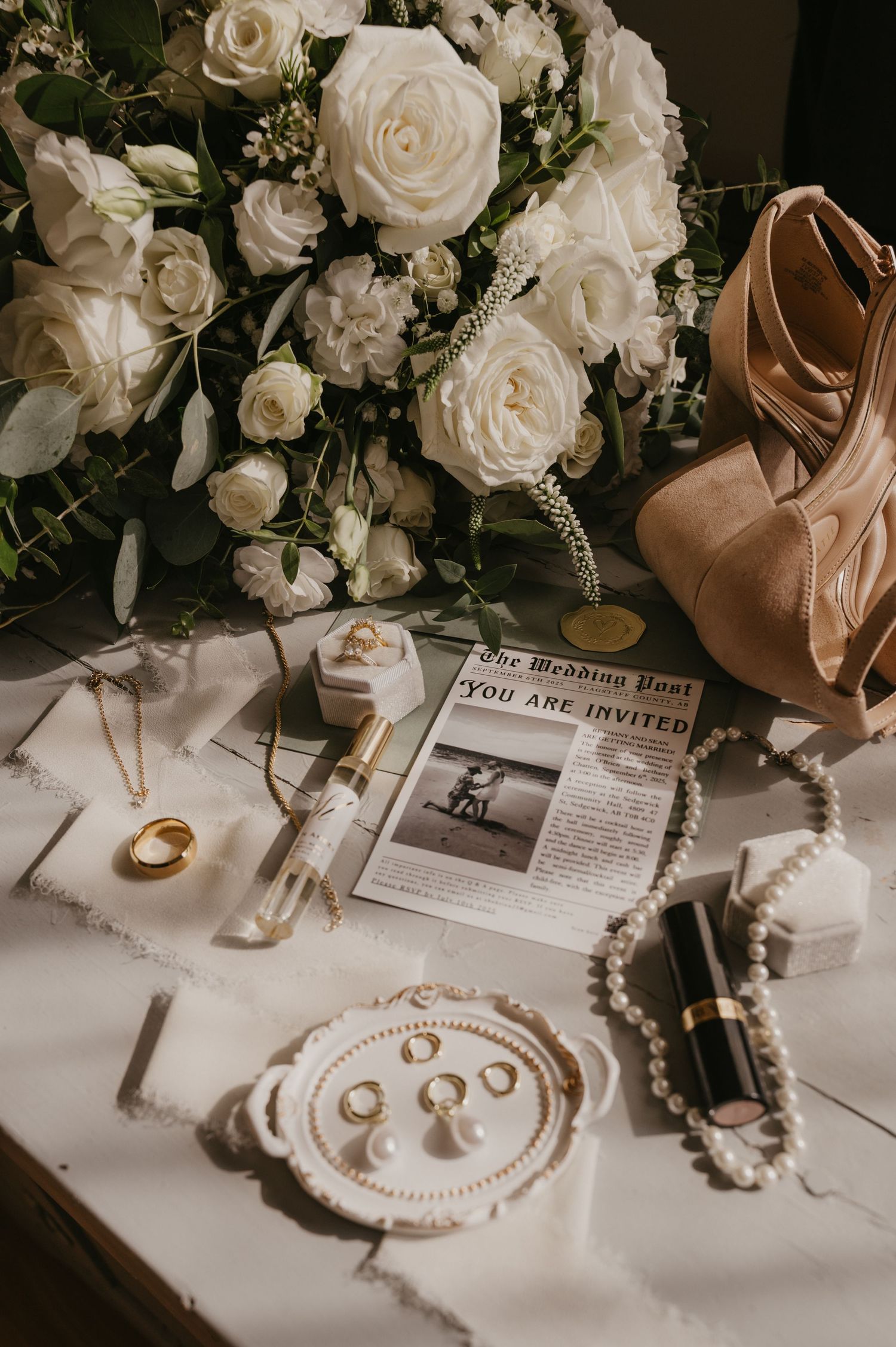 Elegant wedding details with white roses, jewelry, and accessories arranged on a white surface.