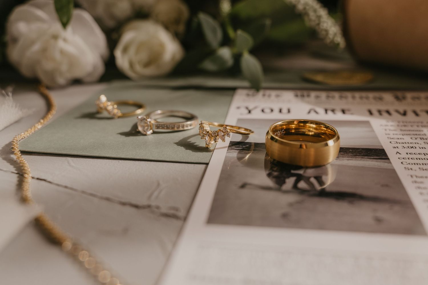 Wedding rings and jewelry arranged artistically on a white surface with roses and printed text in the background.