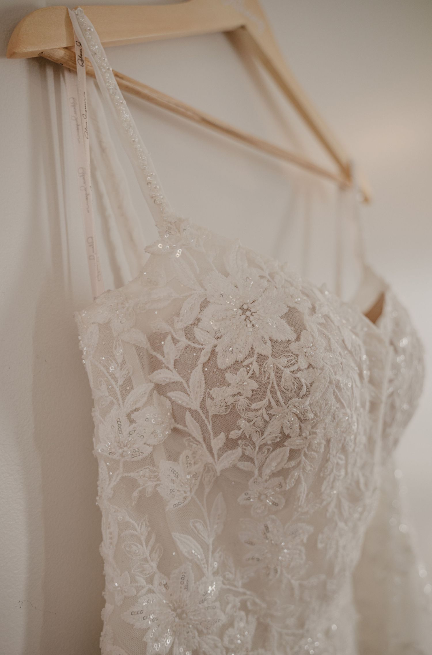 Delicate white lace wedding dress bodice with floral embroidery details hanging on wooden hanger.