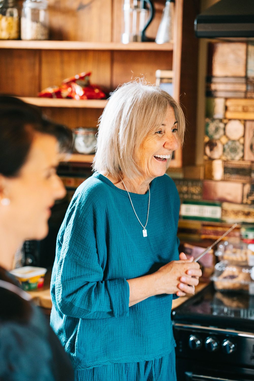 Person in bright teal sweater laughing joyfully in a cozy kitchen setting.