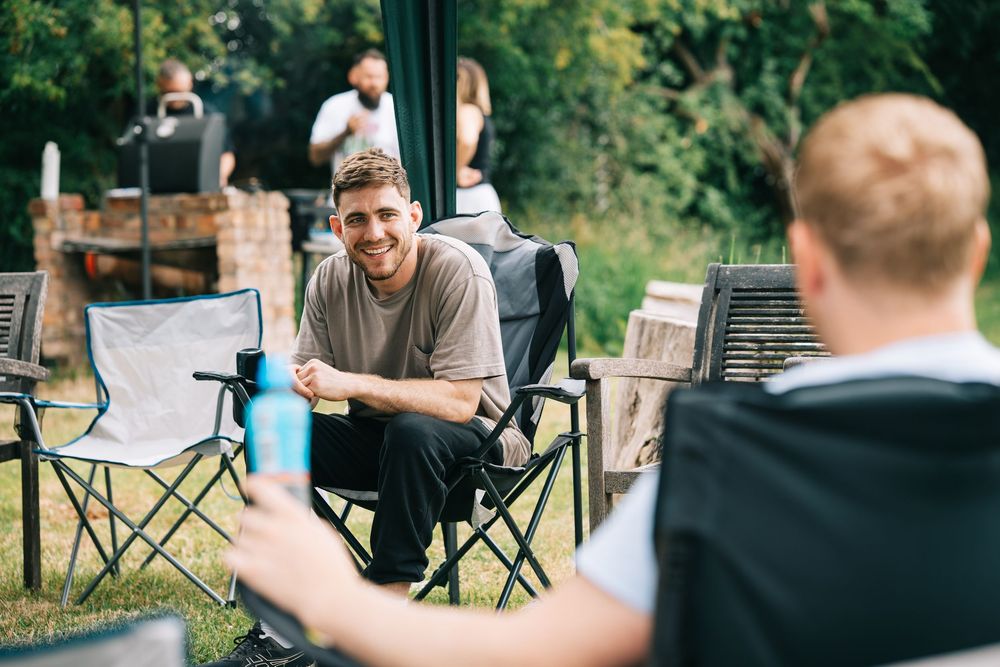 People enjoying an outdoor gathering with camping chairs and drinks in a backyard setting.