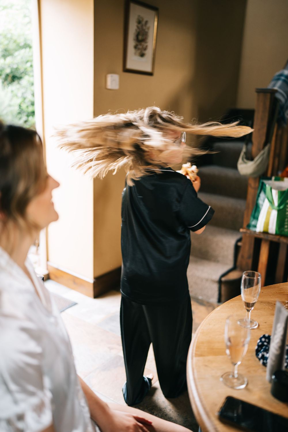 Long blonde hair swirls dramatically in motion during wedding preparations with champagne glass on wooden table.