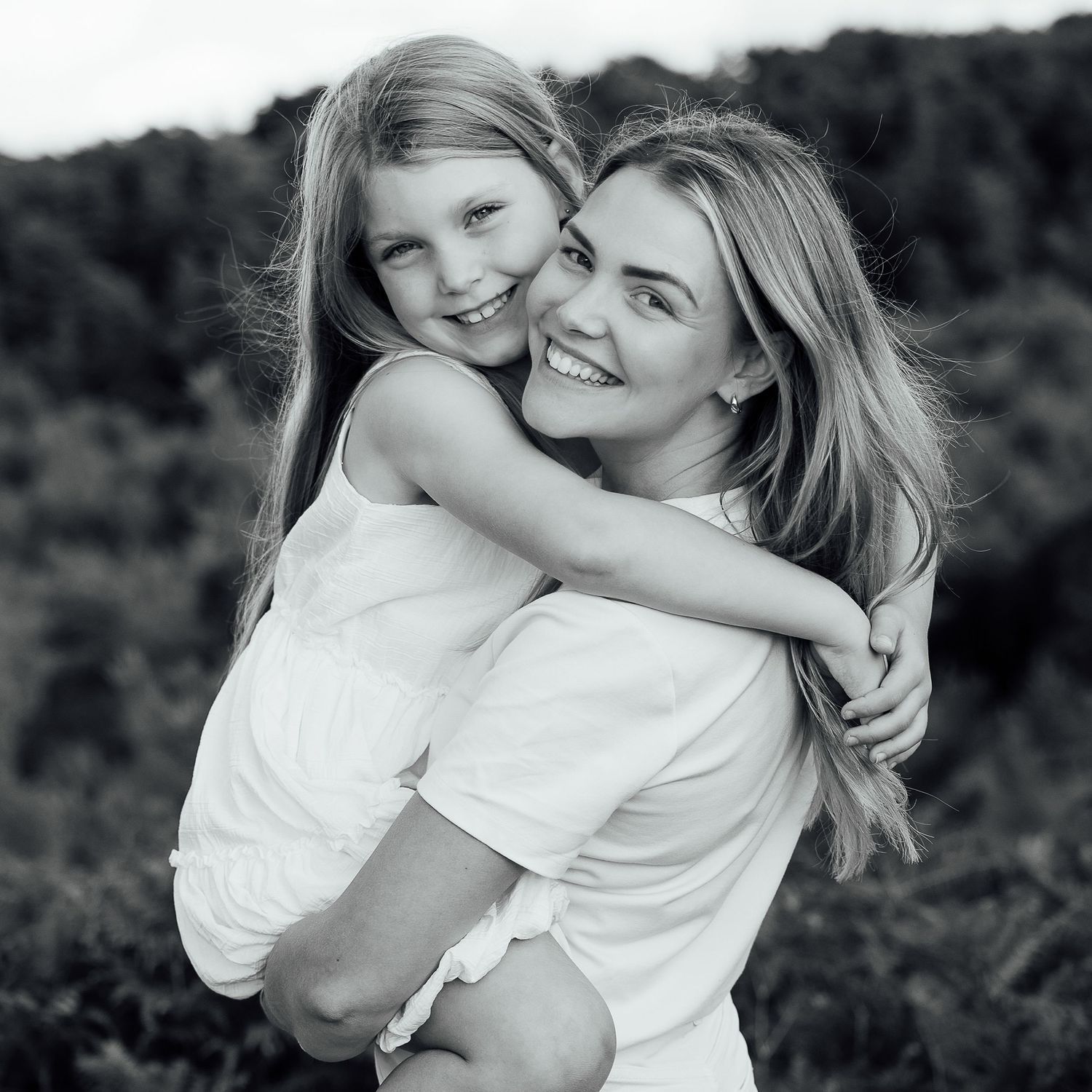 Young mum cuddling her daughter smiling naturally for the camera.  The photo is in black and white.